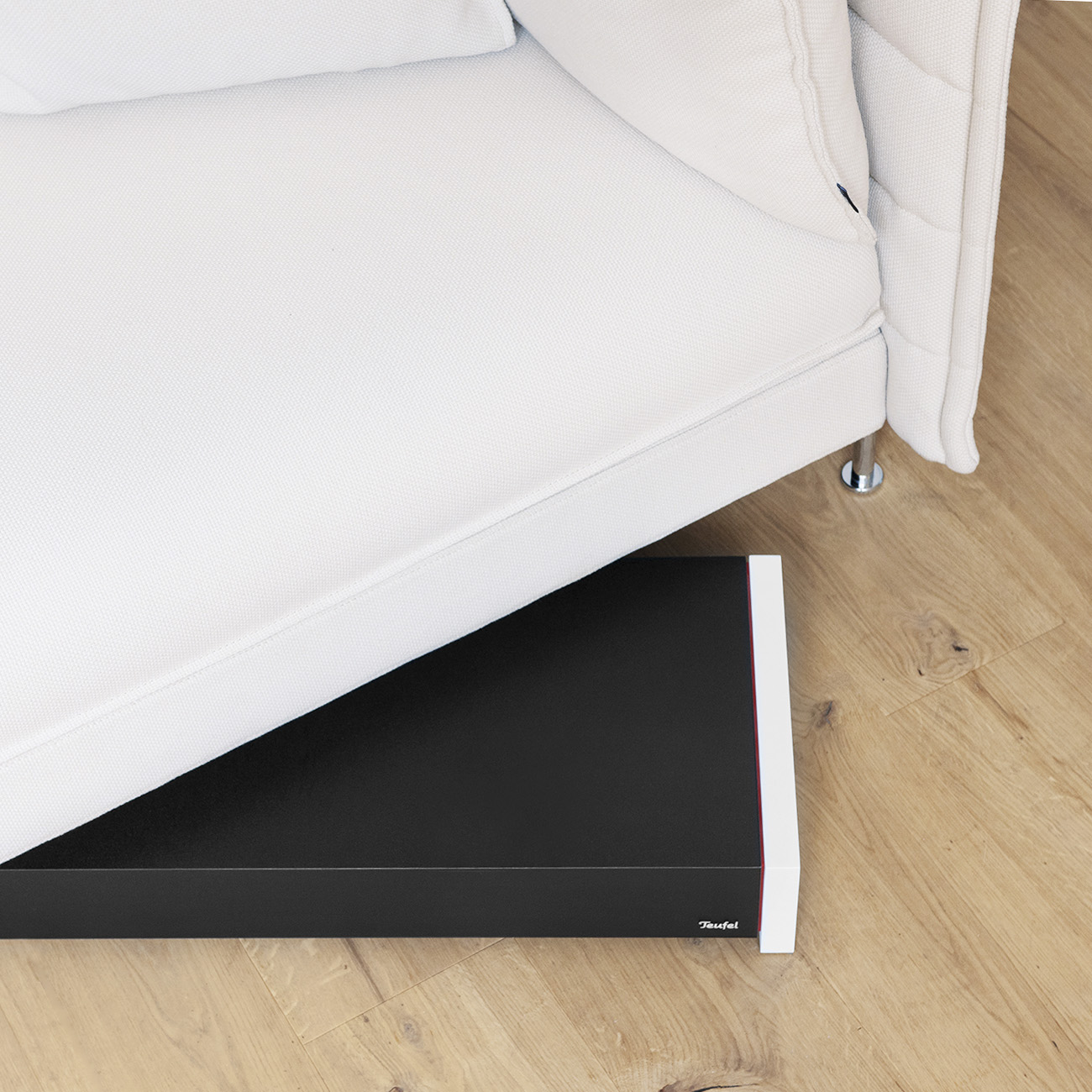 Ein weißes Sofa ruht auf einem schwarzen, flachen Objekt auf Holzboden.