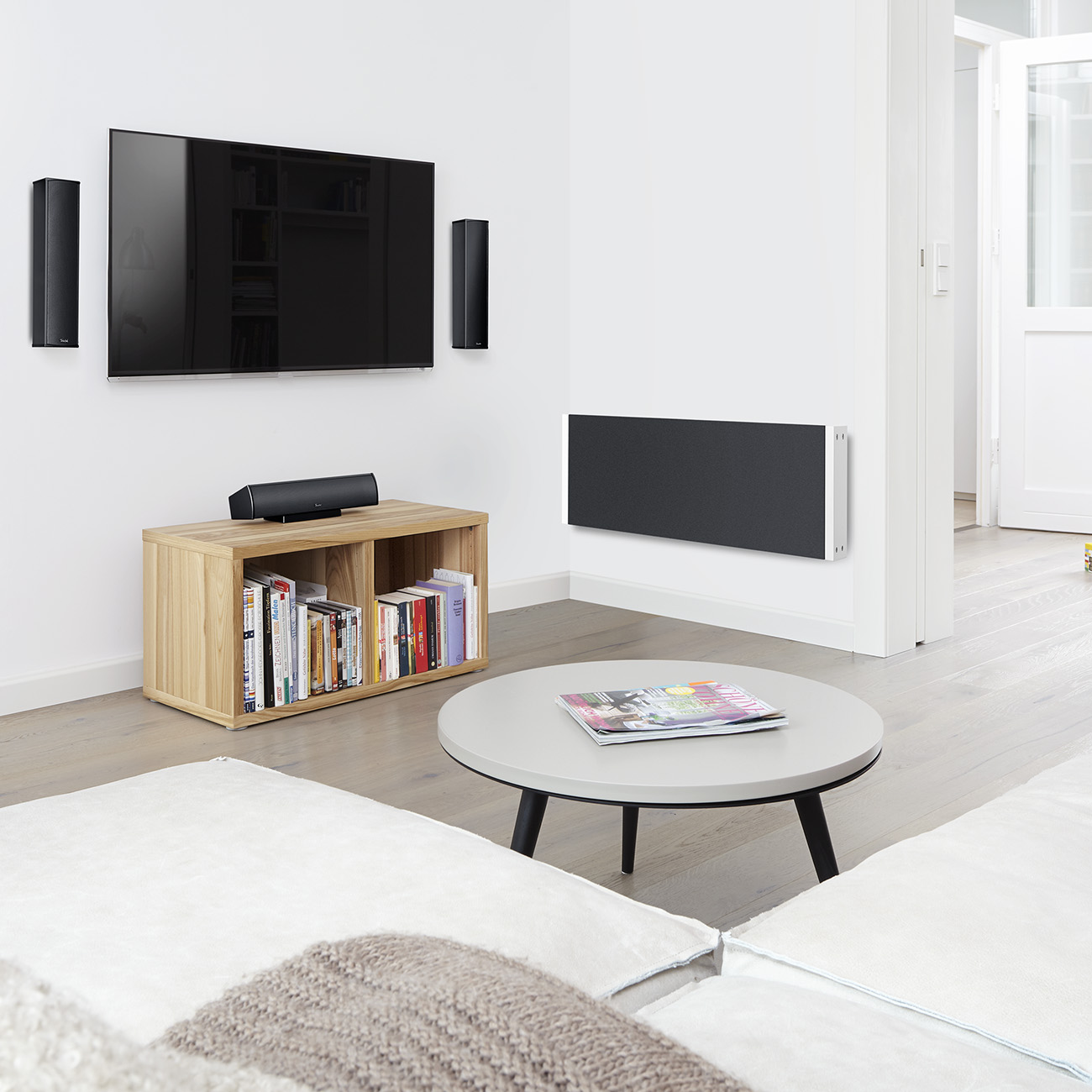Modernes Wohnzimmer mit TV, Lautsprechern, Soundbar, Bücherregal, Couchtisch und Wandheizung.
