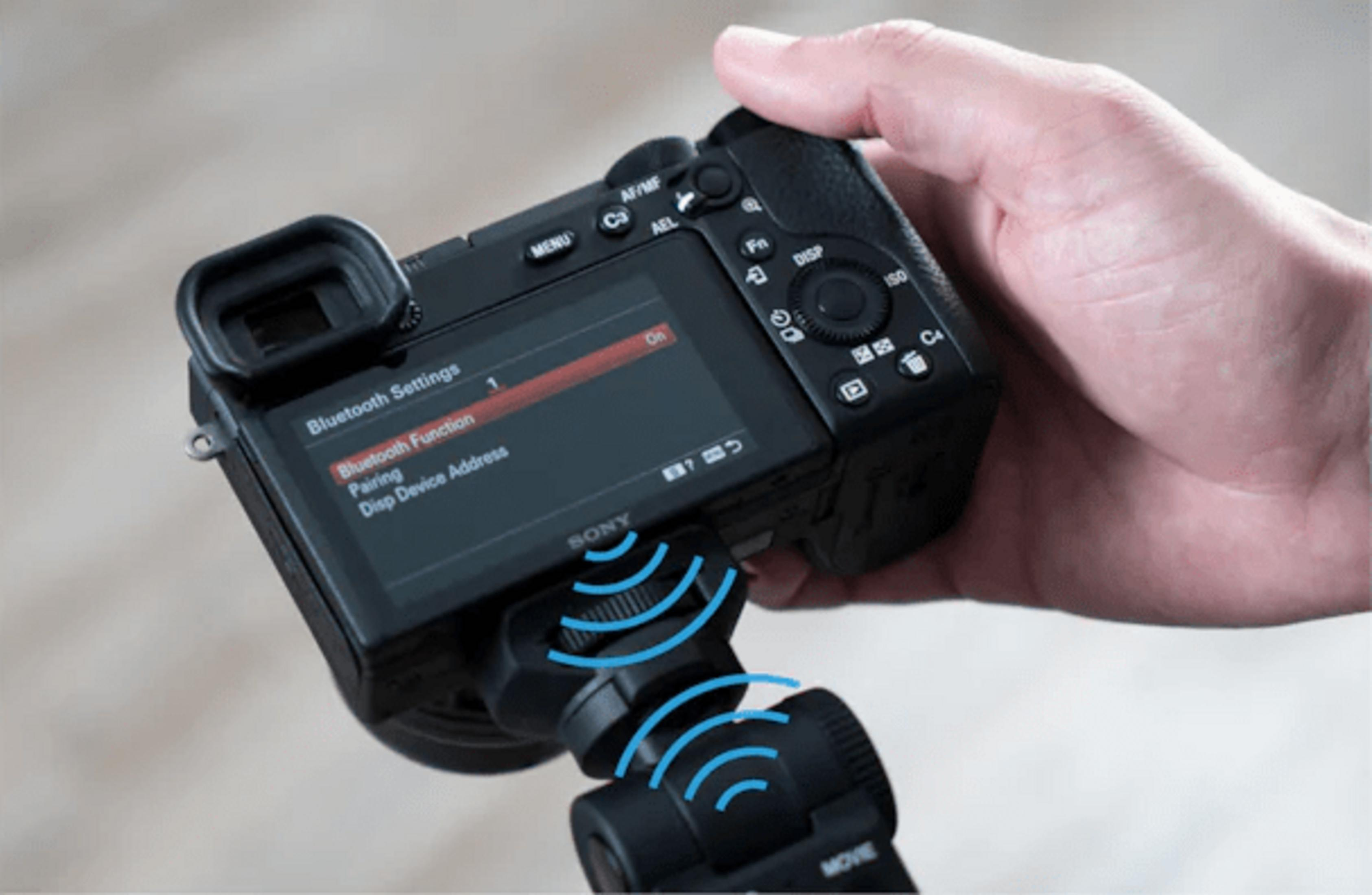 Una mano sostiene una cámara Sony con el menú Bluetooth activado. Ondas azules indican conexión.