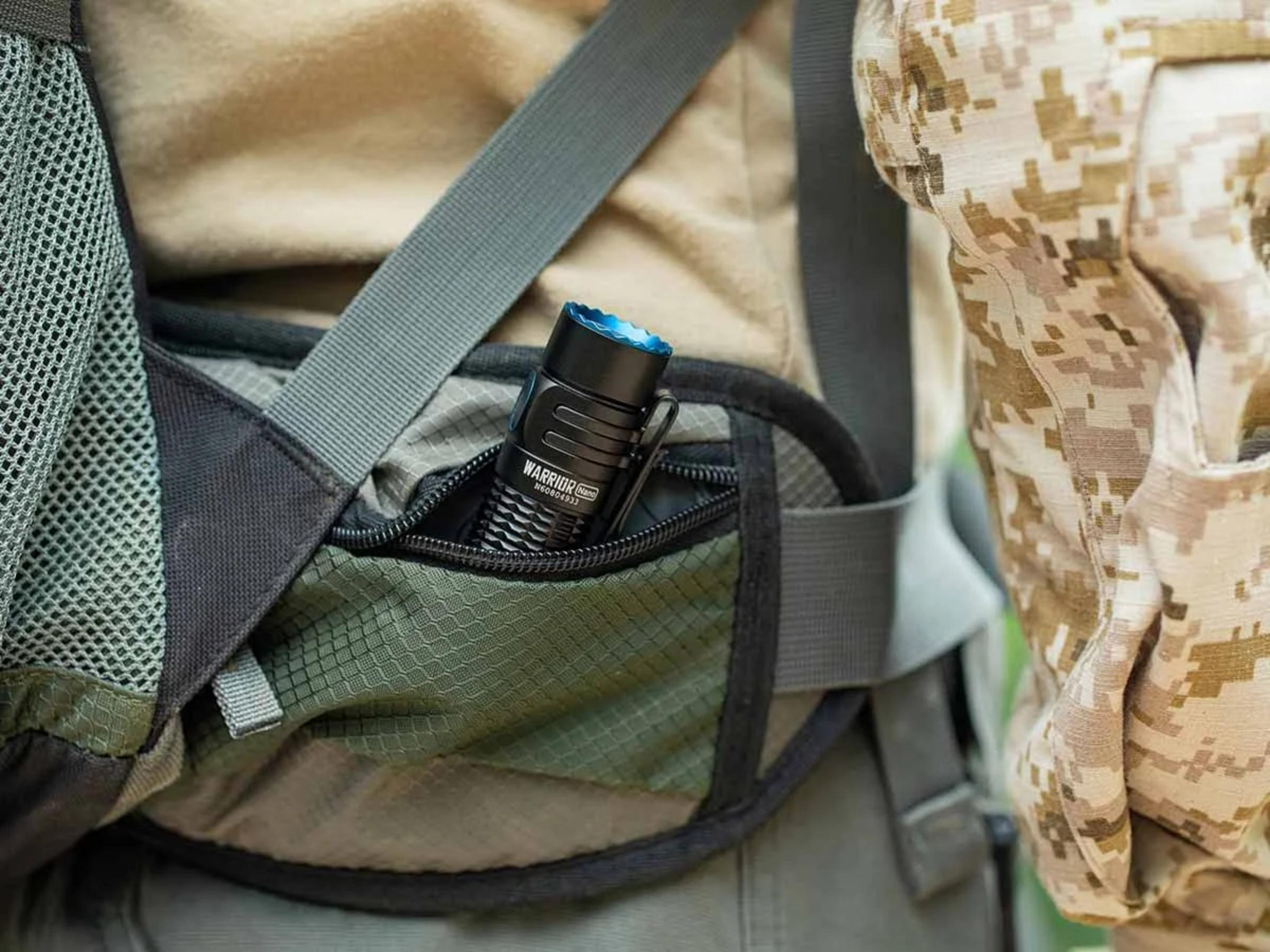 Une lampe torche noire avec un accent bleu est dans la poche d'une veste camouflage.