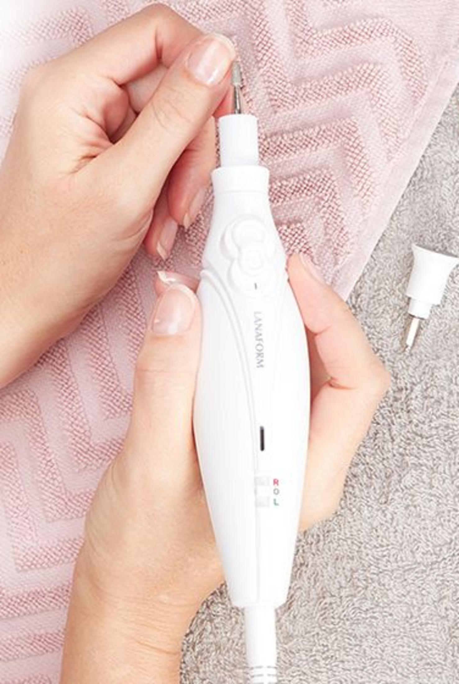 White nail drill held by hands on pink and grey towels.