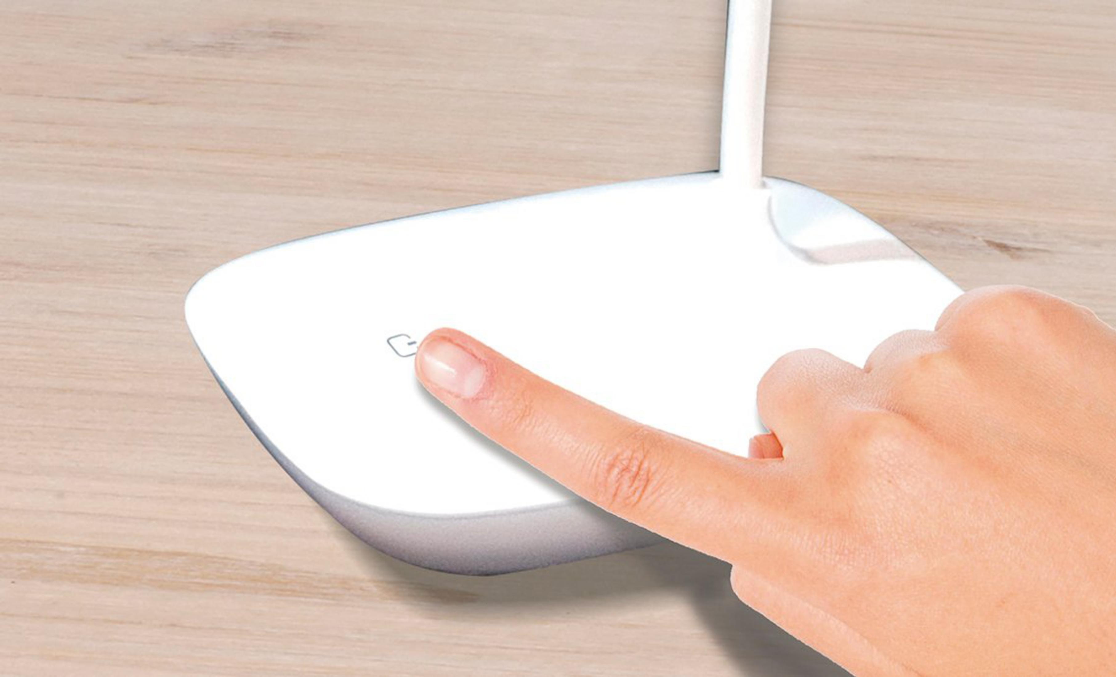 Una mano preme il pulsante di accensione su un dispositivo bianco su tavolo.