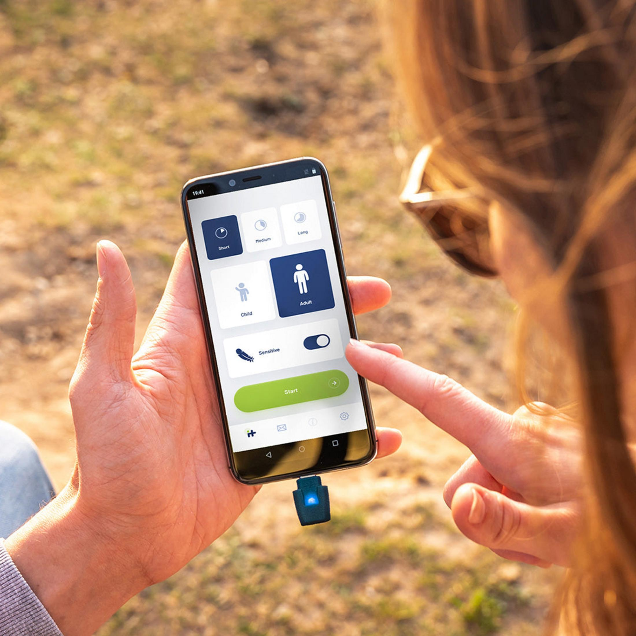 Una mano sostiene un teléfono inteligente que muestra una aplicación con opciones cortas, medianas, largas, infantiles y de adulto.