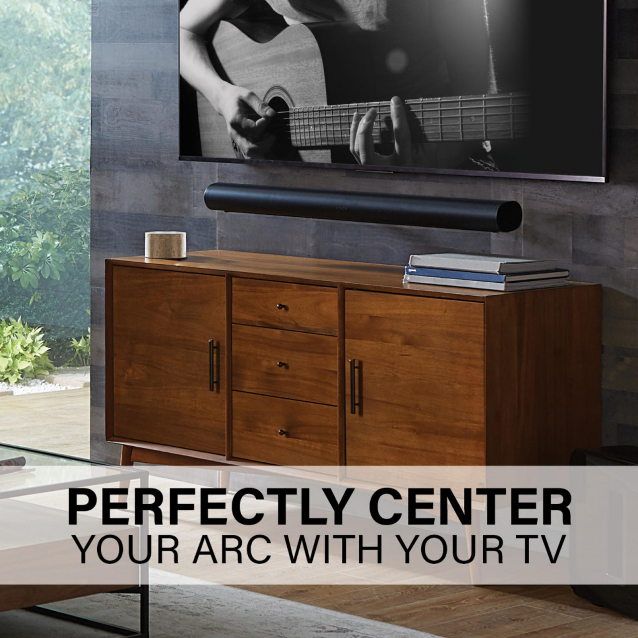 Een man speelt gitaar voor een tv met een soundbar.
