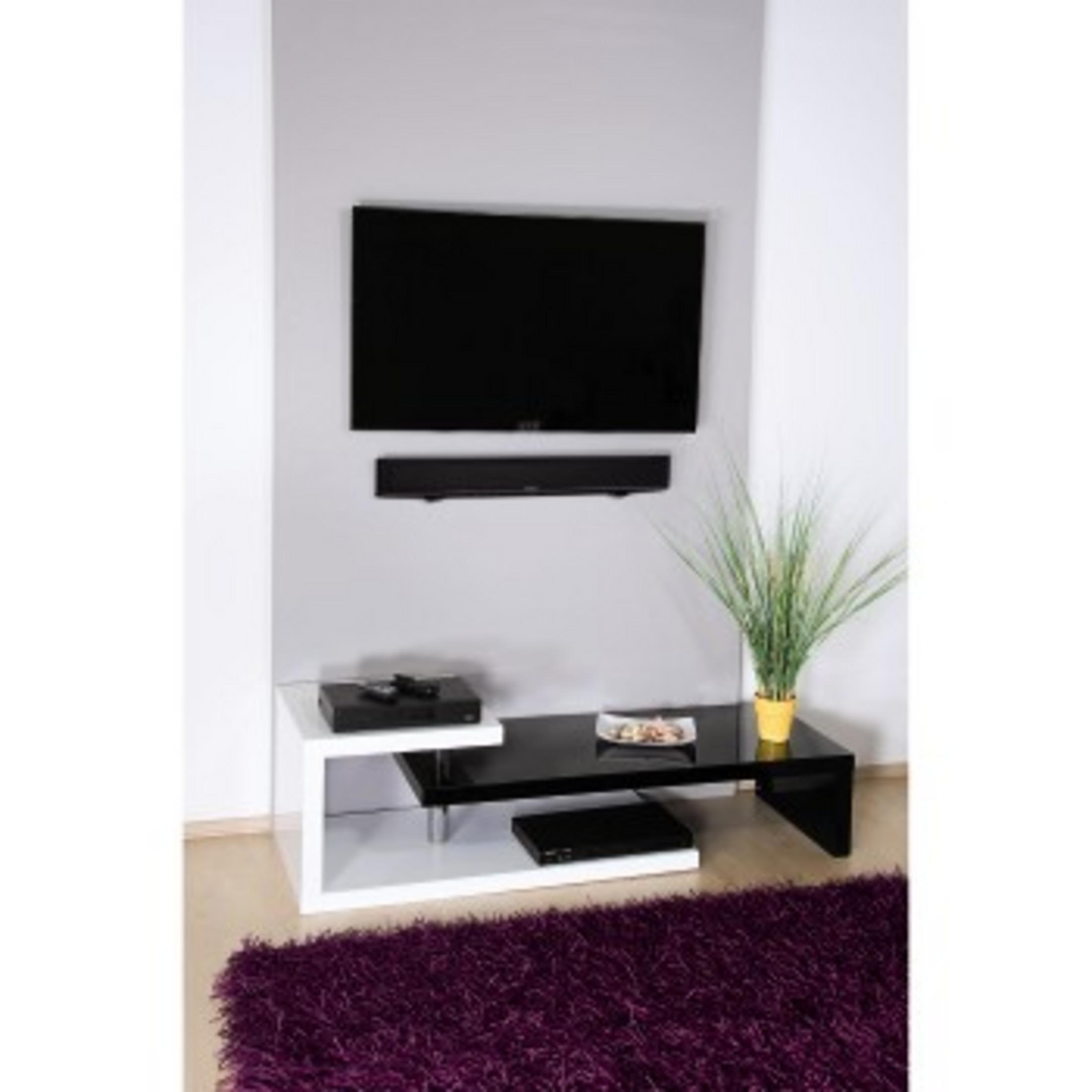 Schwarzer Fernseher über schwarzer Soundbar, weiß-schwarzer Tisch mit Geräten und Pflanze.
