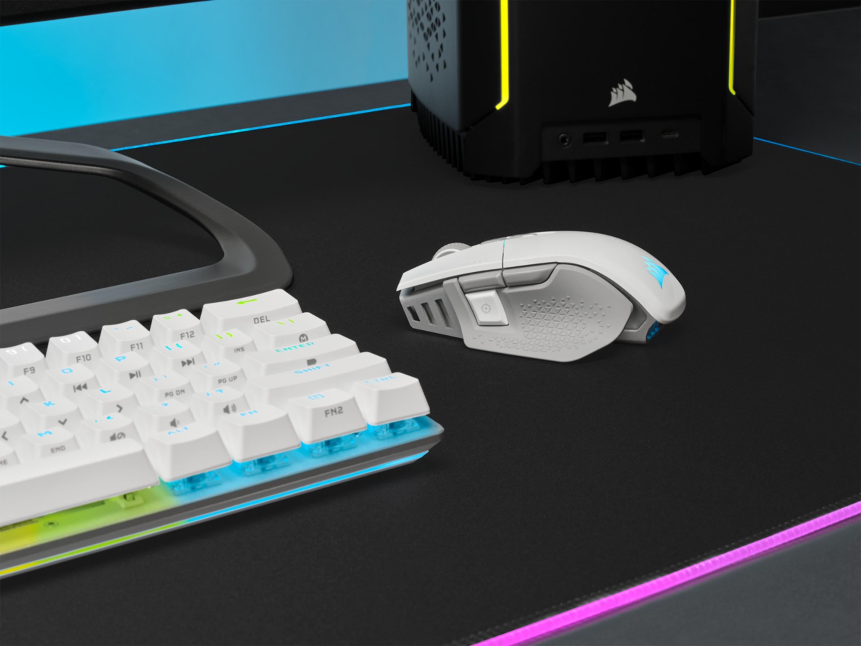 Un ratón y teclado gaming blancos descansan sobre una alfombrilla negra con iluminación RGB.