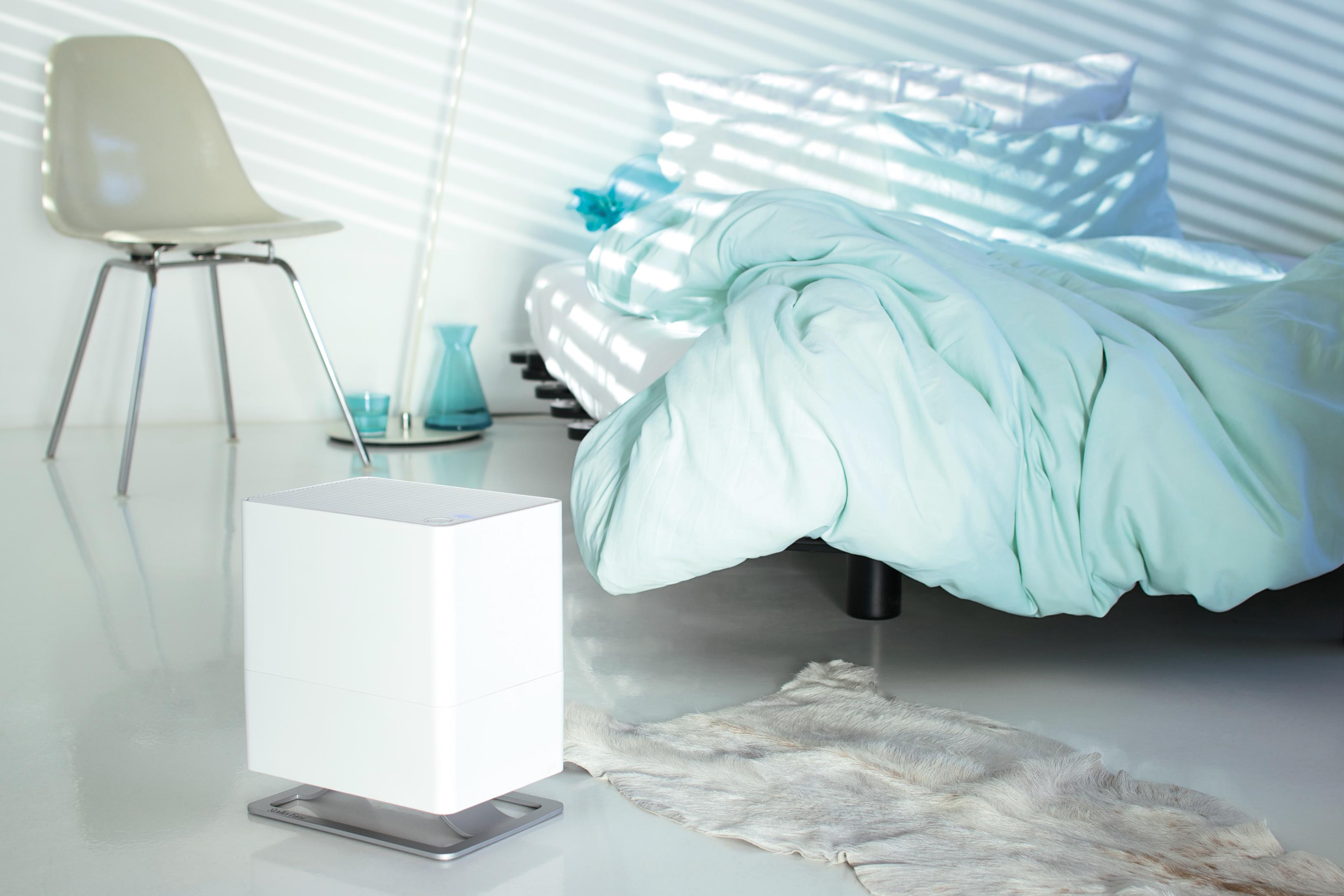 A white humidifier sits next to a bed with mint green bedding. A chair is nearby.