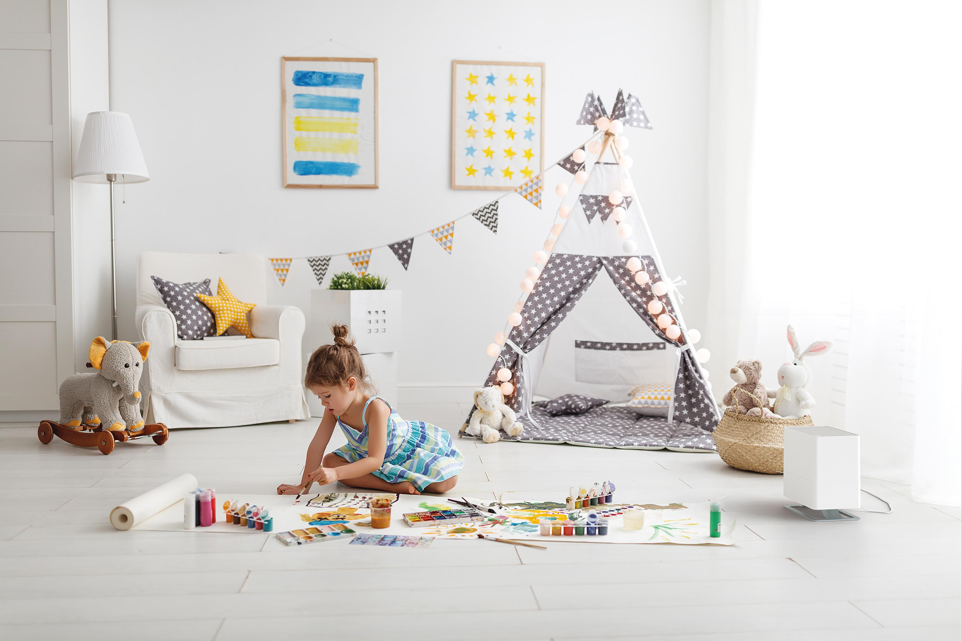 A girl paints on the floor in a bright room with toys.