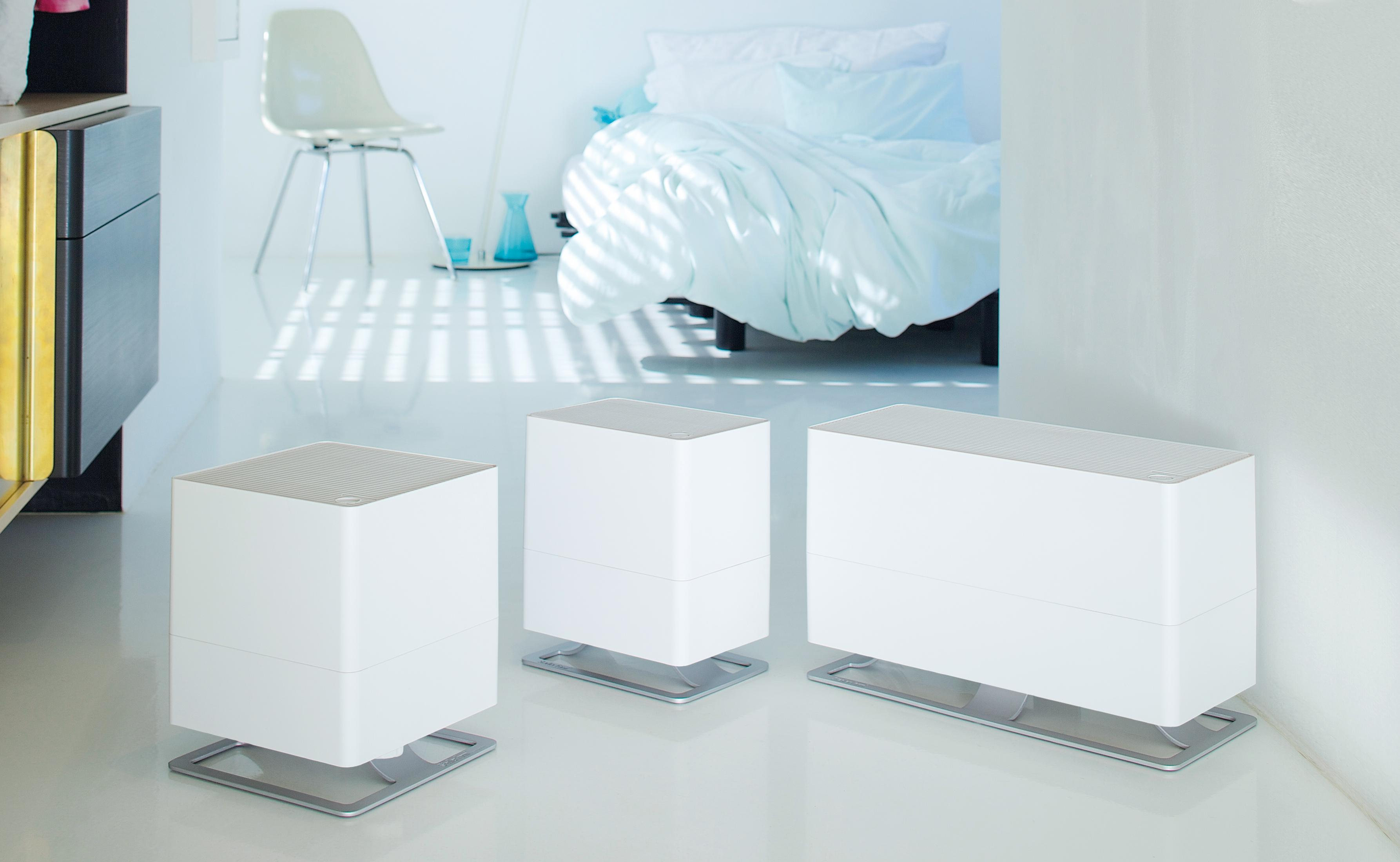 Three white humidifiers sit on a shiny floor in a minimalist room.