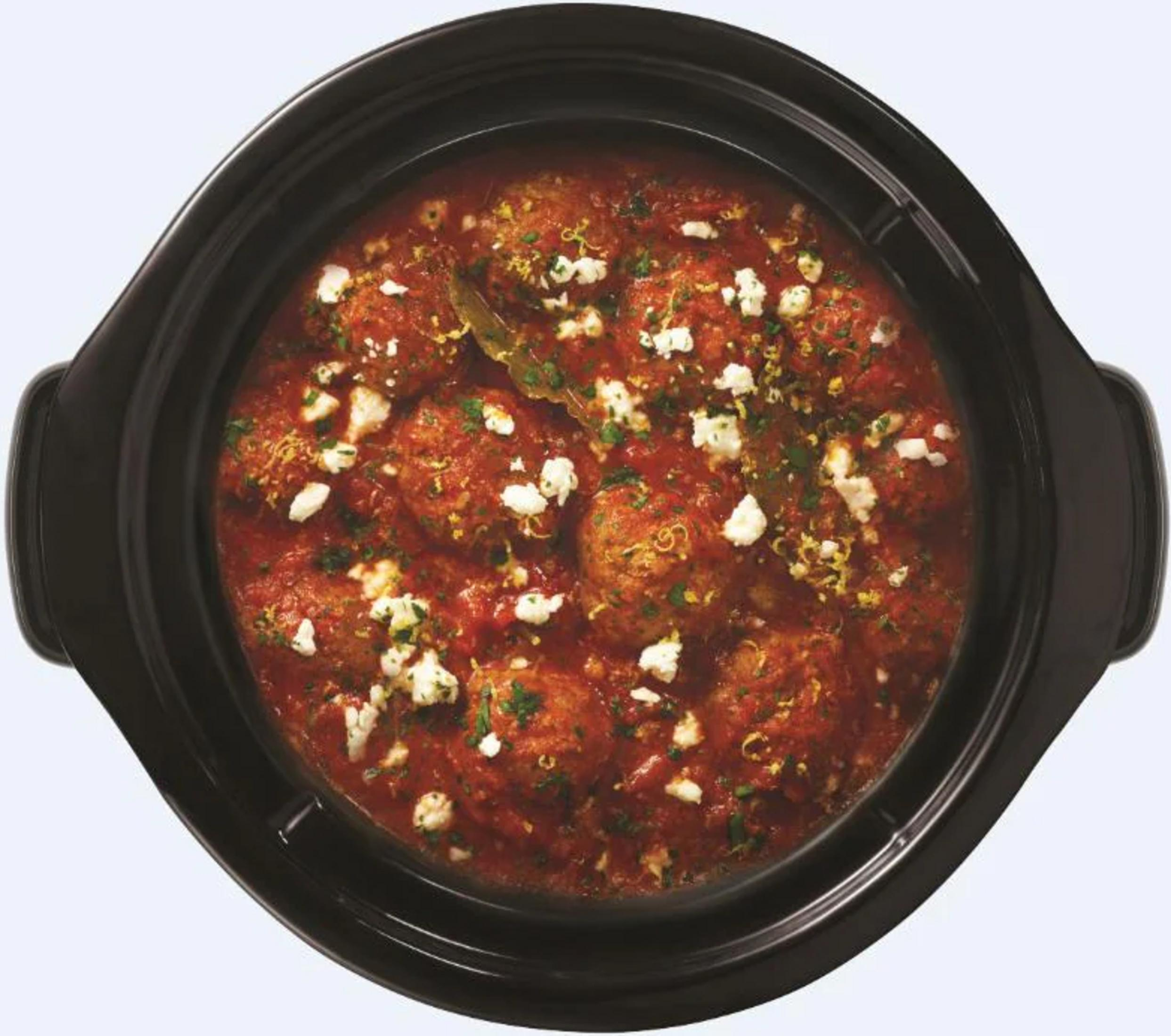 Fleischbällchen in Tomatensoße mit Feta und Kräutern in einem schwarzen Topf.