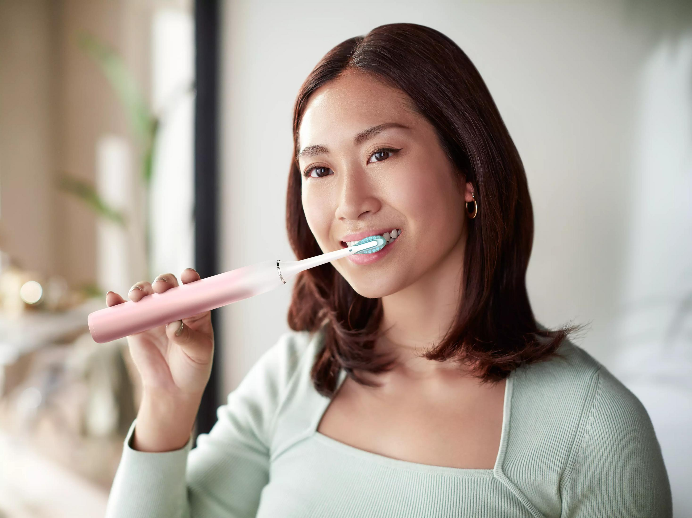 Una donna si lava i denti con uno spazzolino elettrico rosa.