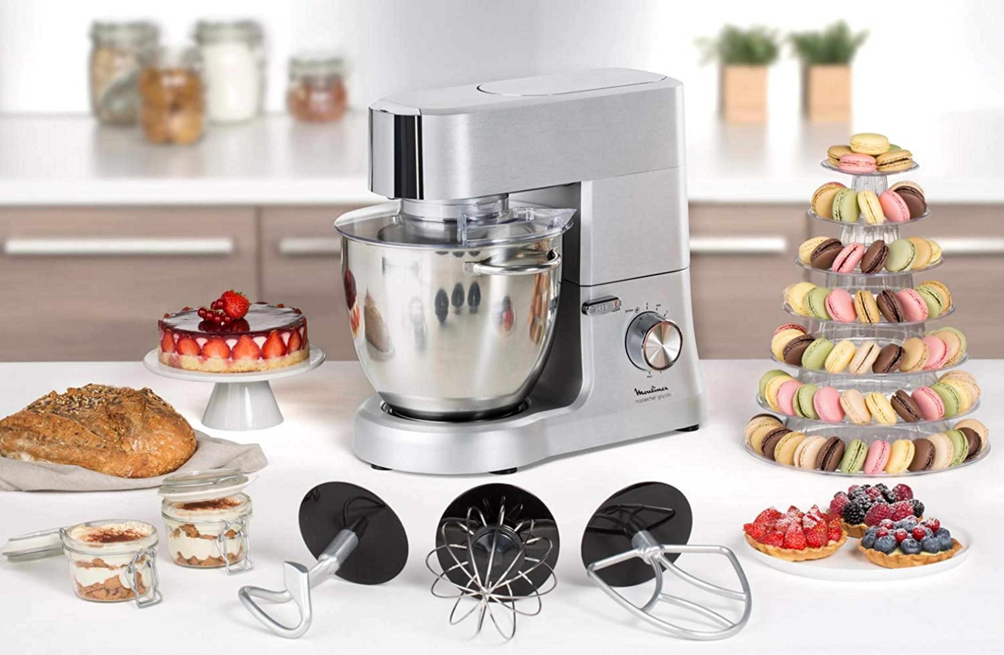 Ein silberner Küchenmixer mit Schüssel, daneben Brot, Kuchen, Macarons und Törtchen.