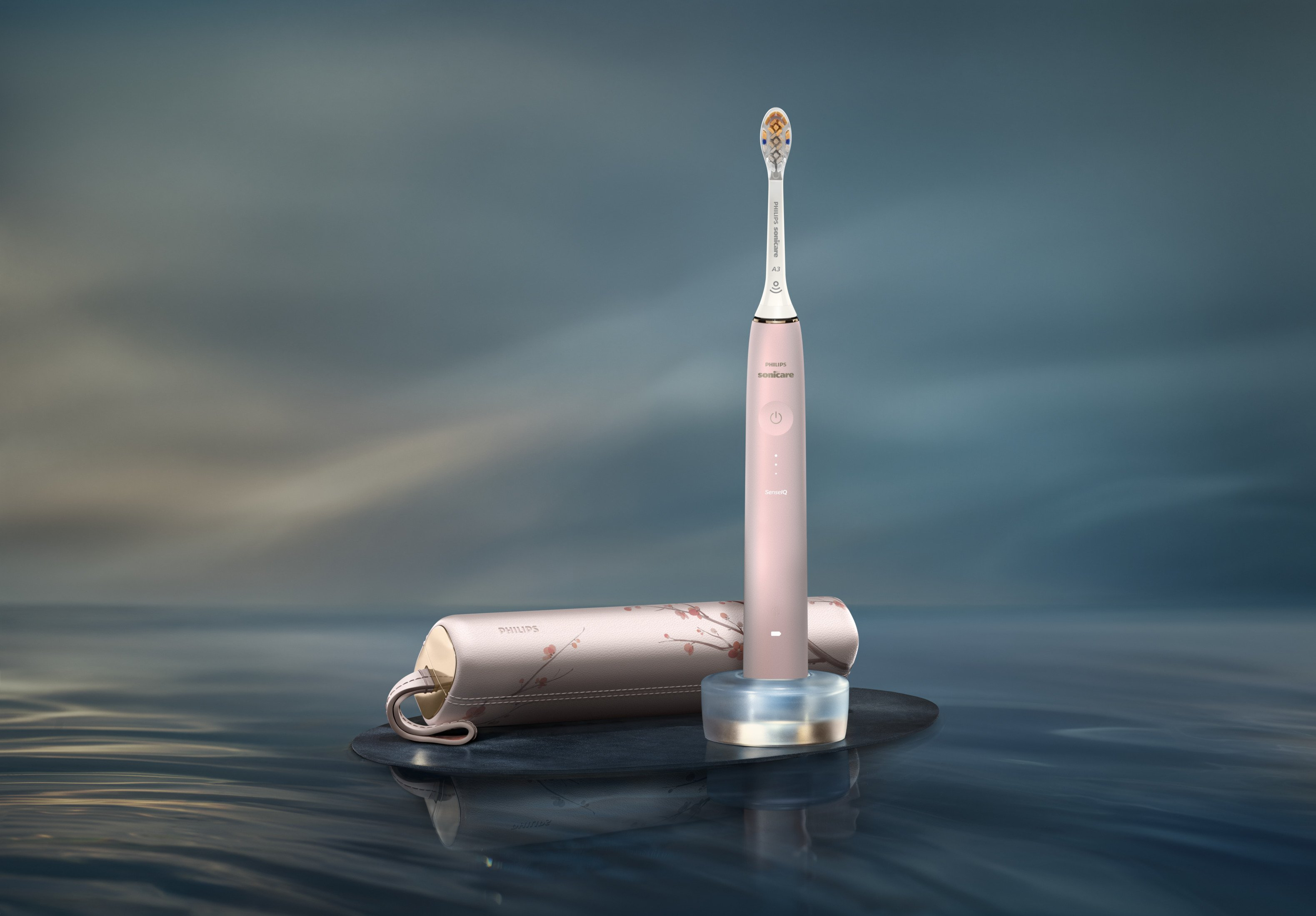 Eine rosafarbene elektrische Zahnbürste mit Ladehalterung und Etui auf einer Wasseroberfläche.