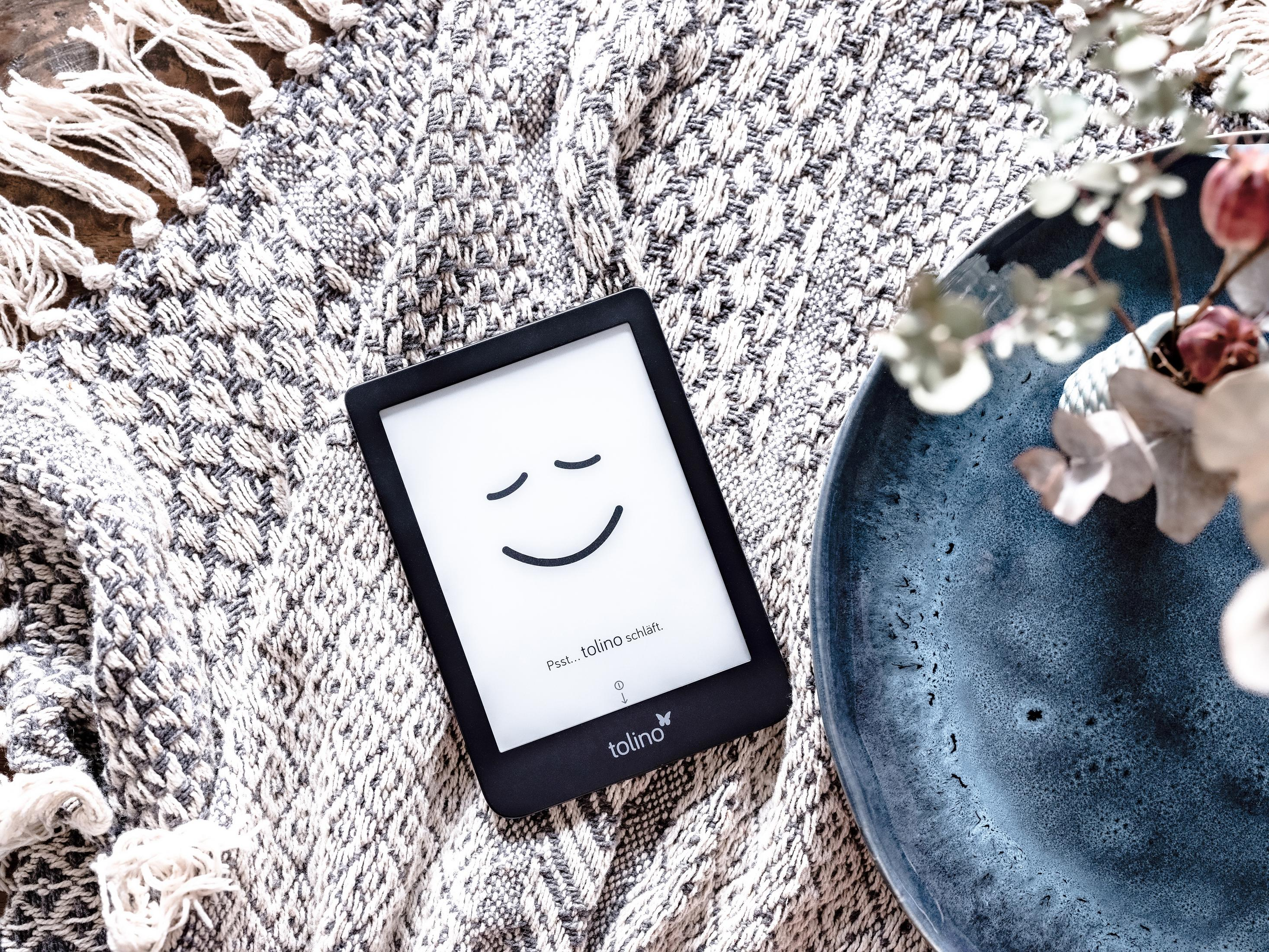 Ein E-Reader mit lächelndem Gesicht auf einer Decke neben einer blauen Schale.