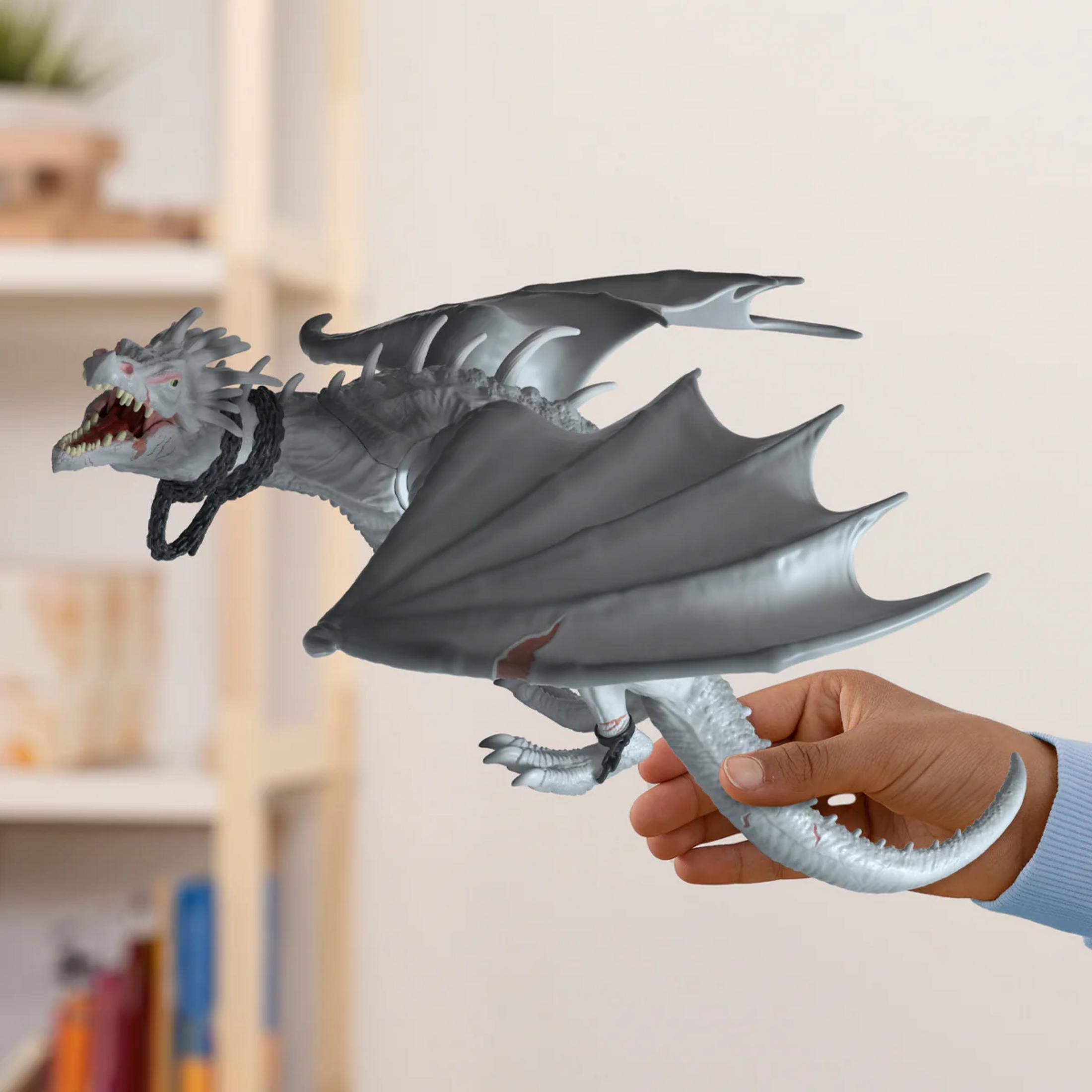 Giocattolo drago grigio con catena al collo tenuto da una mano.