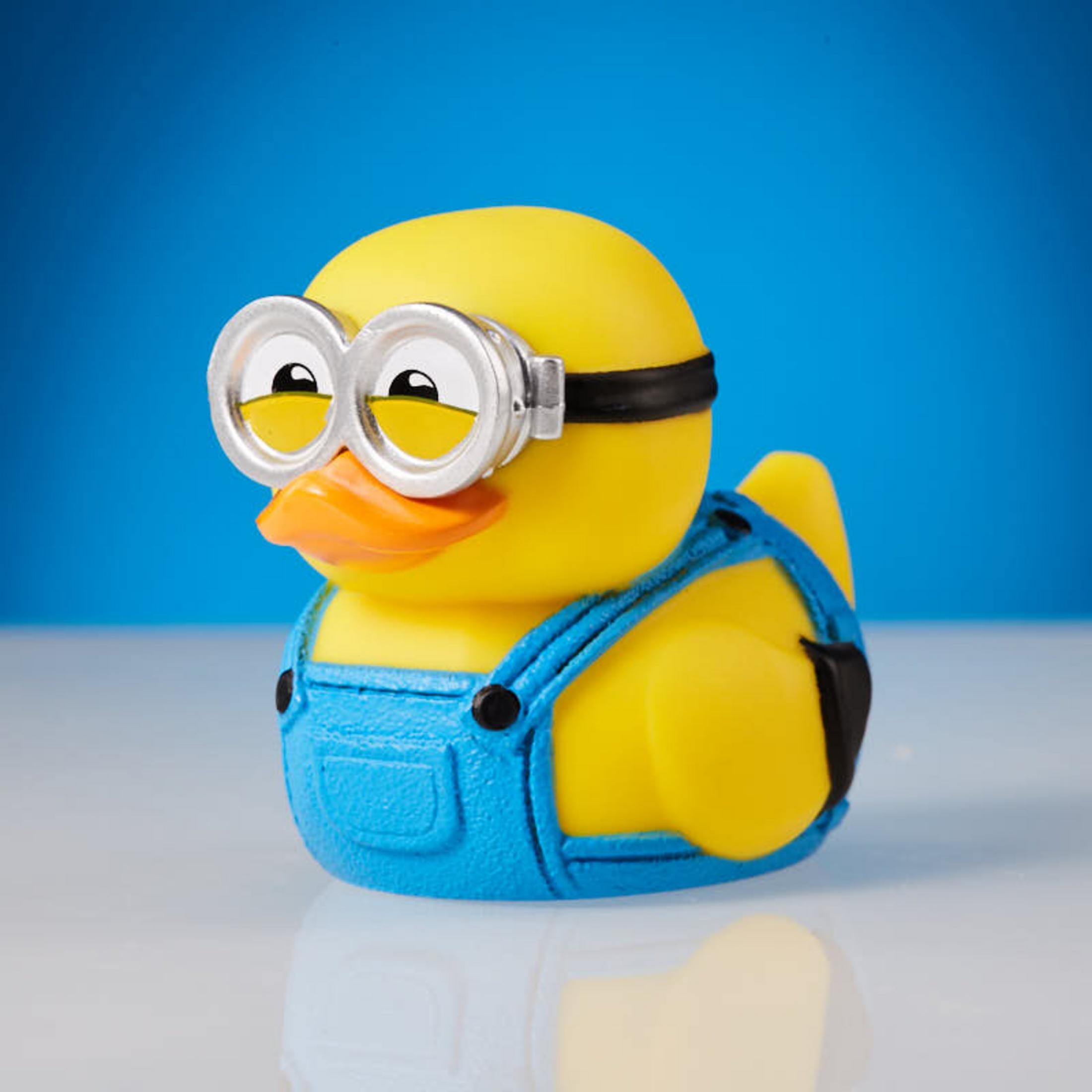 Gelbe Quietscheente mit blauer Latzhose und Minion-Brille auf blauem Hintergrund.