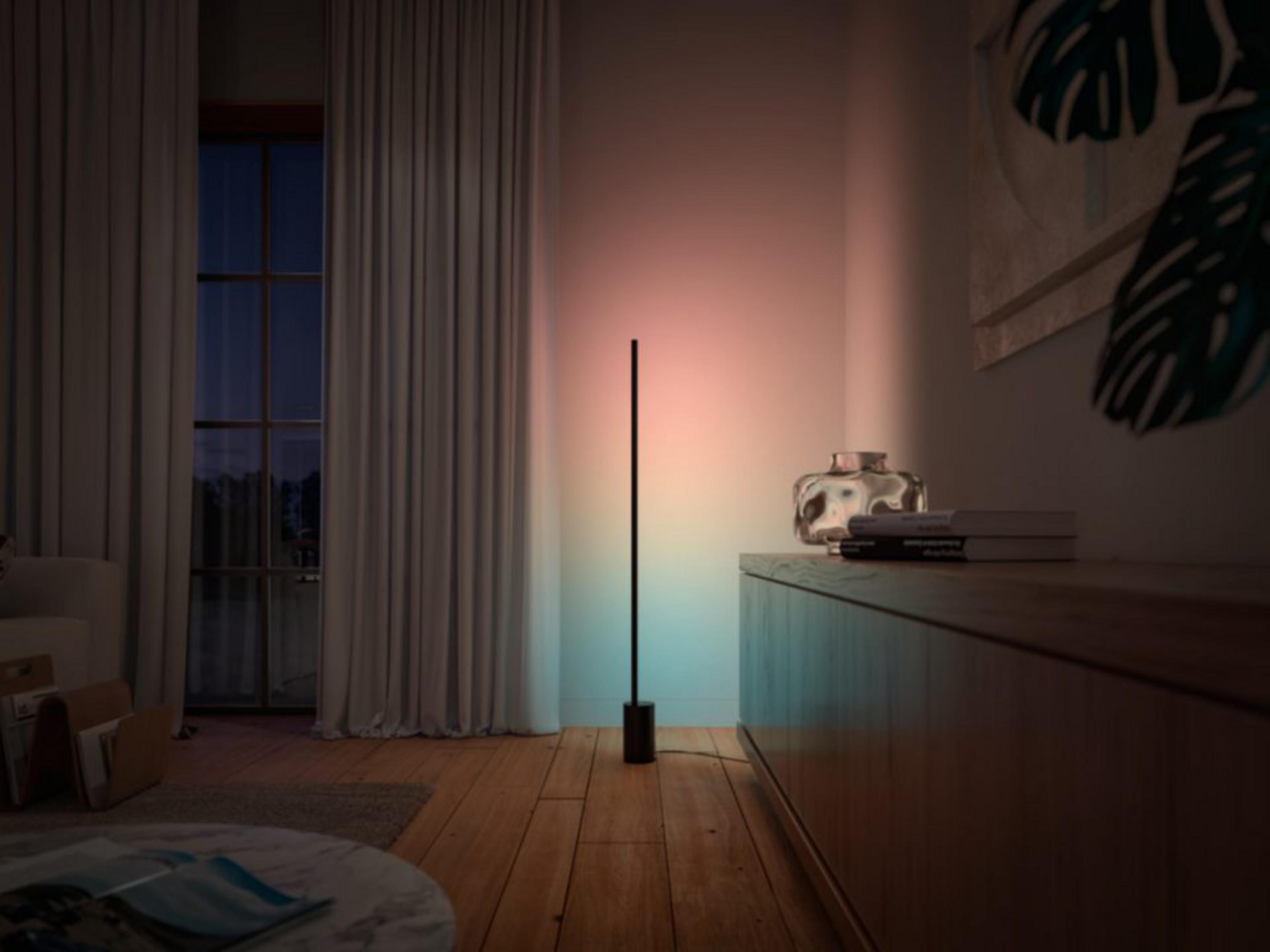 Minimalist bir lambader, pembe ve mavi tonlarıyla bir duvarı aydınlatıyor.