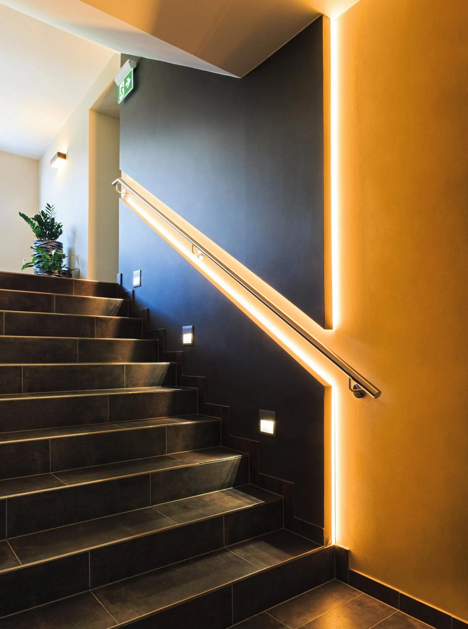 Moderne Treppe mit dunklen Stufen, Geländer und Akzentbeleuchtung.