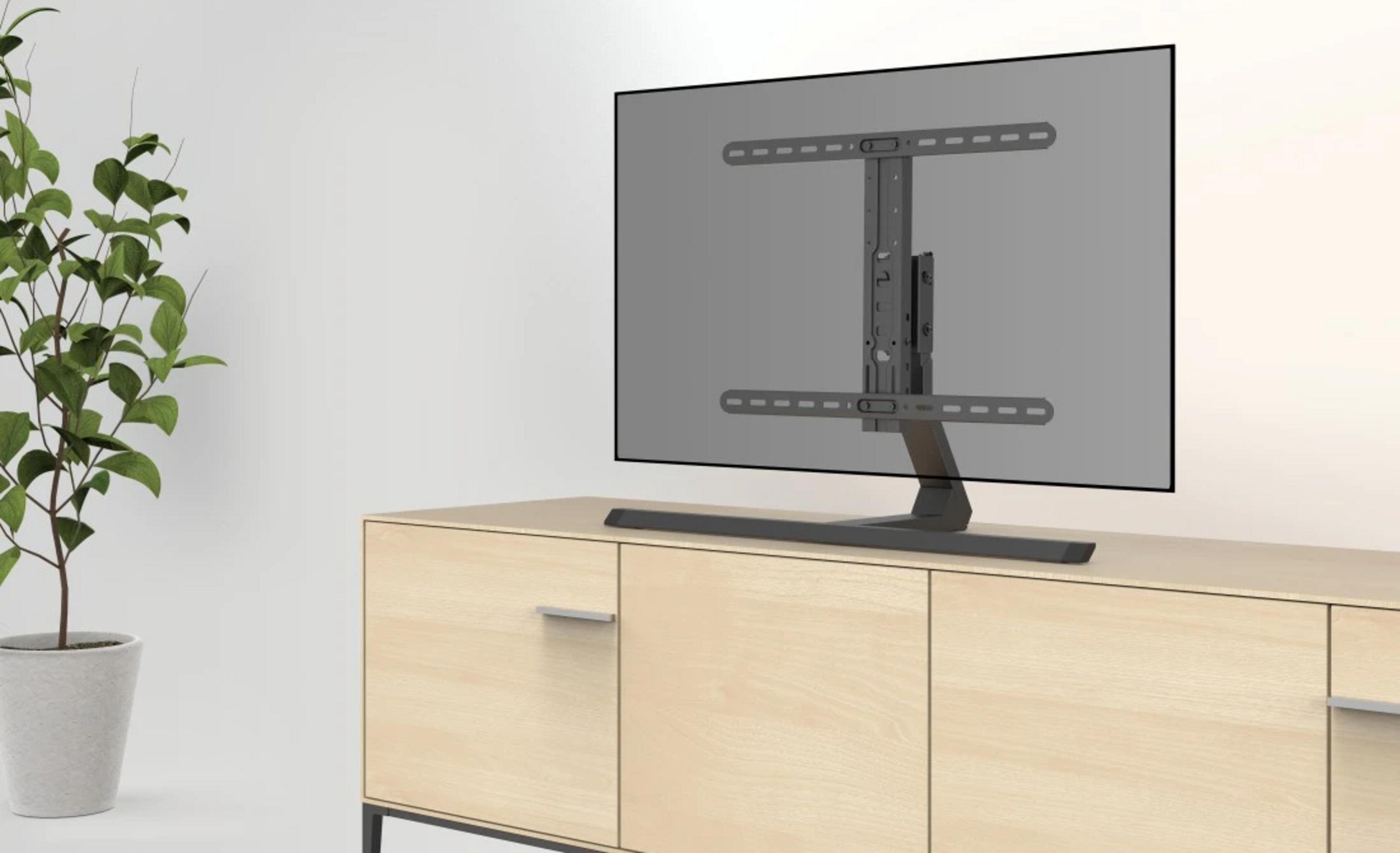 Un supporto TV con base in metallo scuro poggia su un mobile in legno chiaro accanto a una pianta in vaso.