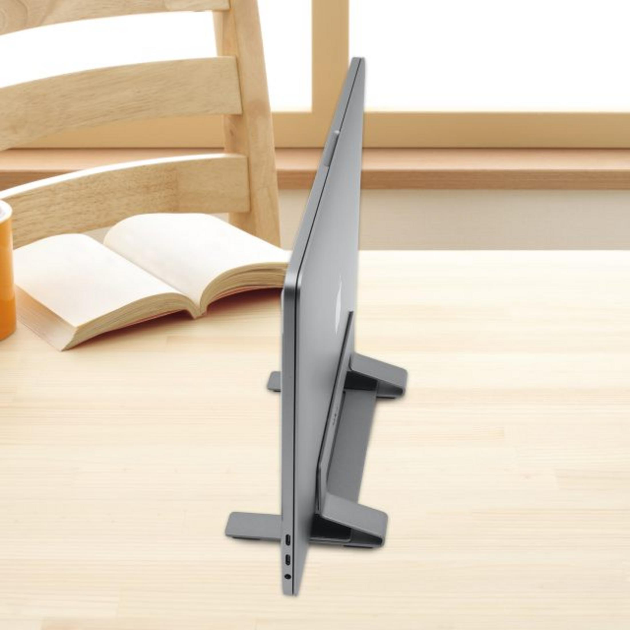 Ein graues Laptop auf einem Ständer, daneben ein offenes Buch und eine Tasse.