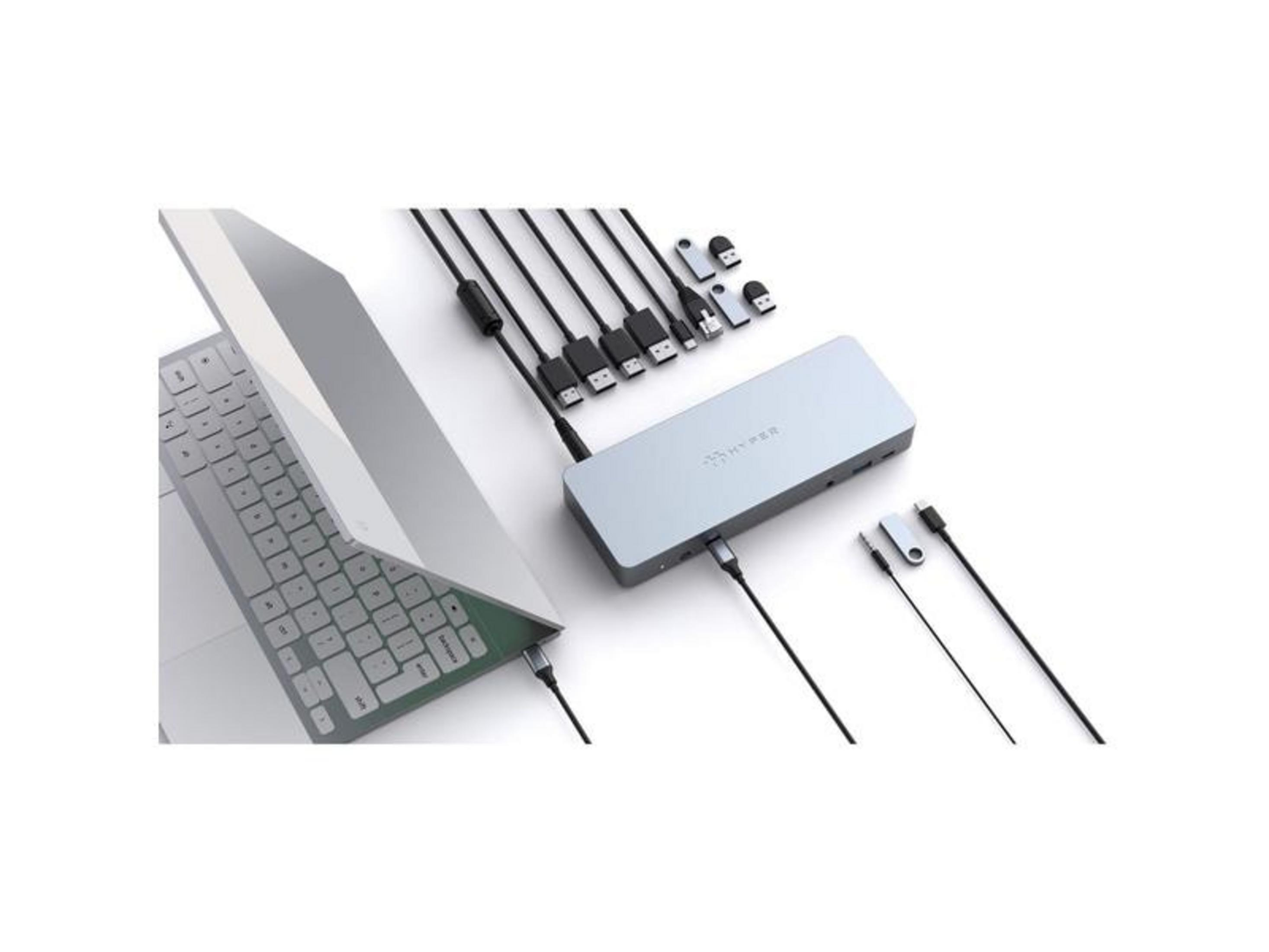 Una base USB-C plateada con cables y adaptadores junto a un portátil.