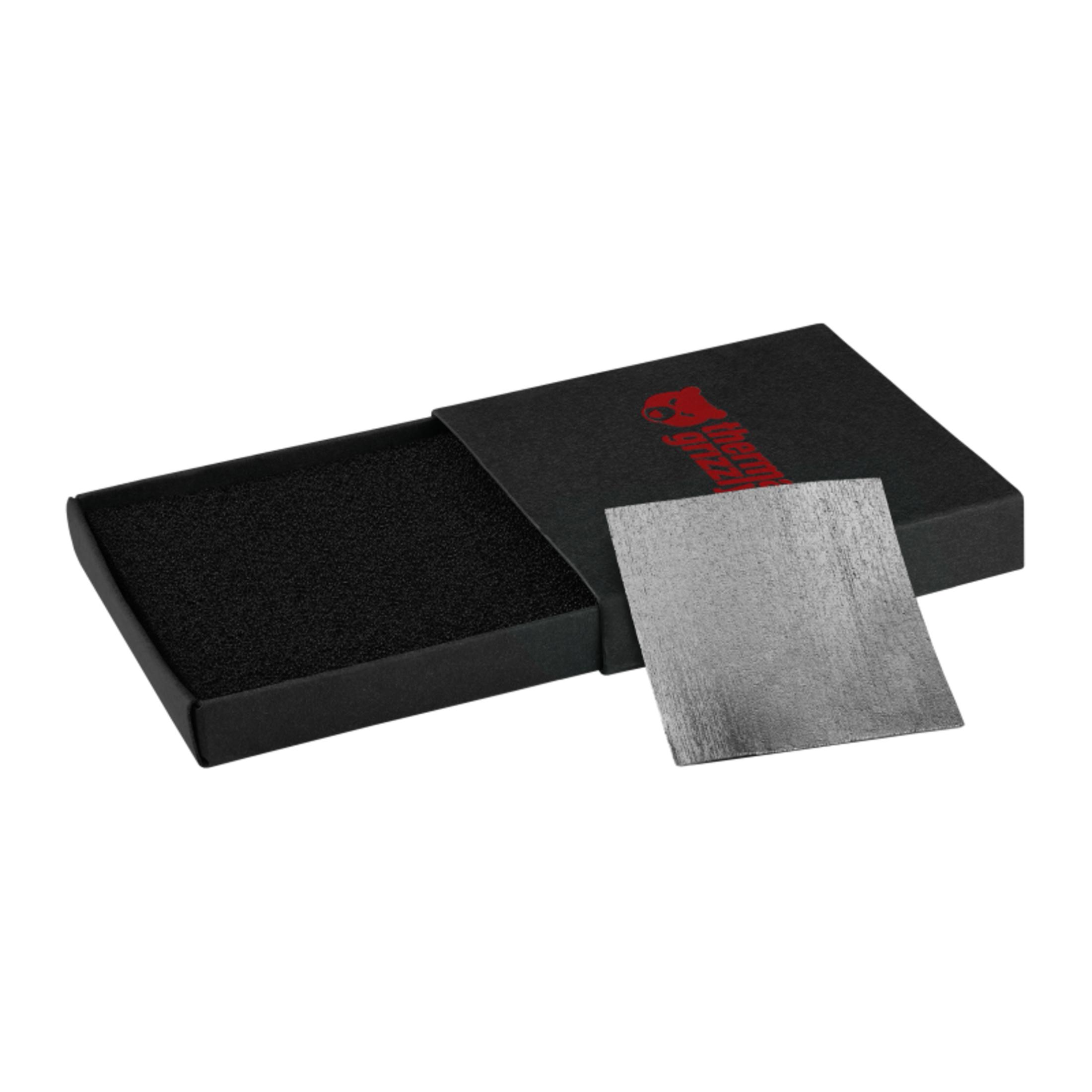 Ein schwarzer Karton mit rotem Logo, darin eine graue Metallplatte.