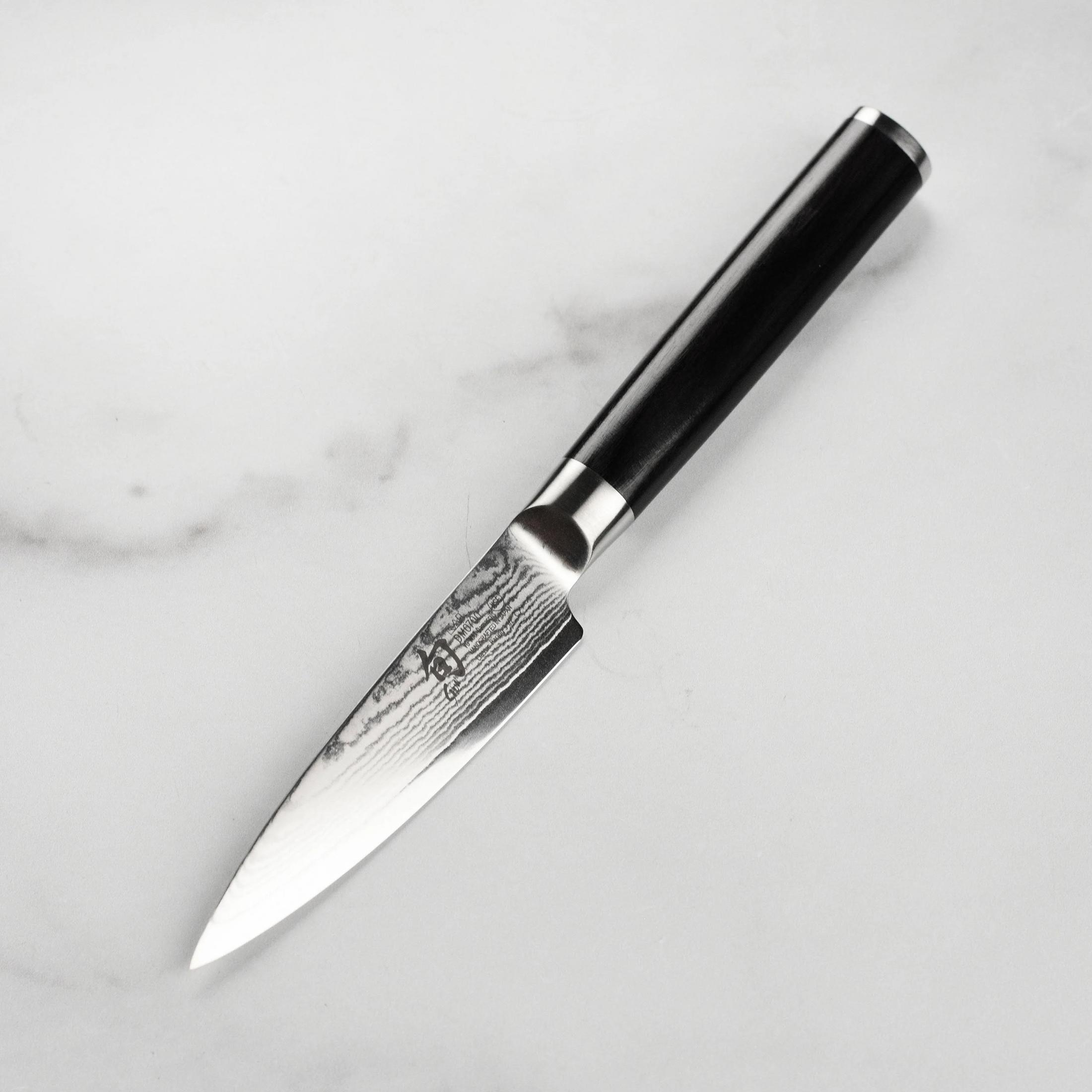 Un cuchillo de acero Damasco con mango negro descansa sobre mármol.