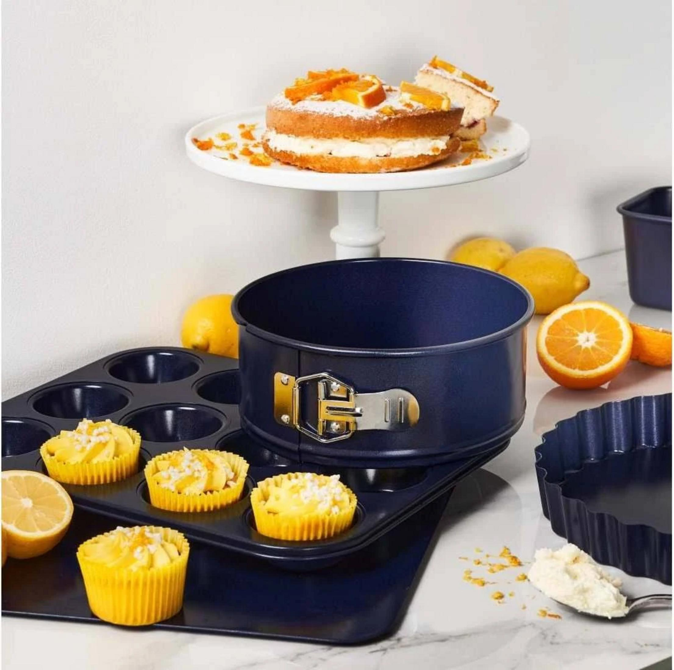 Ein Kuchen mit Orangen, Muffins und Backformen auf einem Marmortisch.