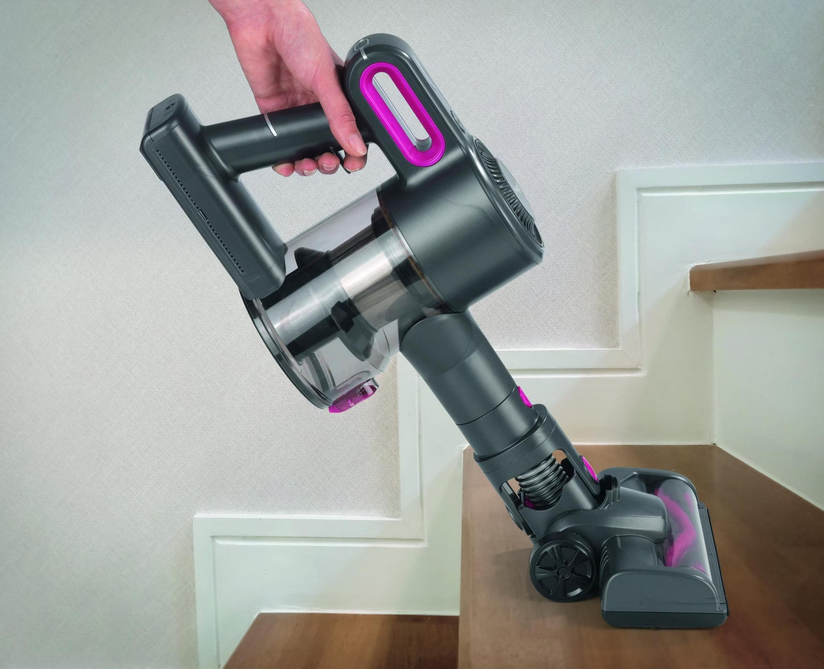 Hand hält dunklen Staubsauger mit pinken Akzenten auf Holzstufe.