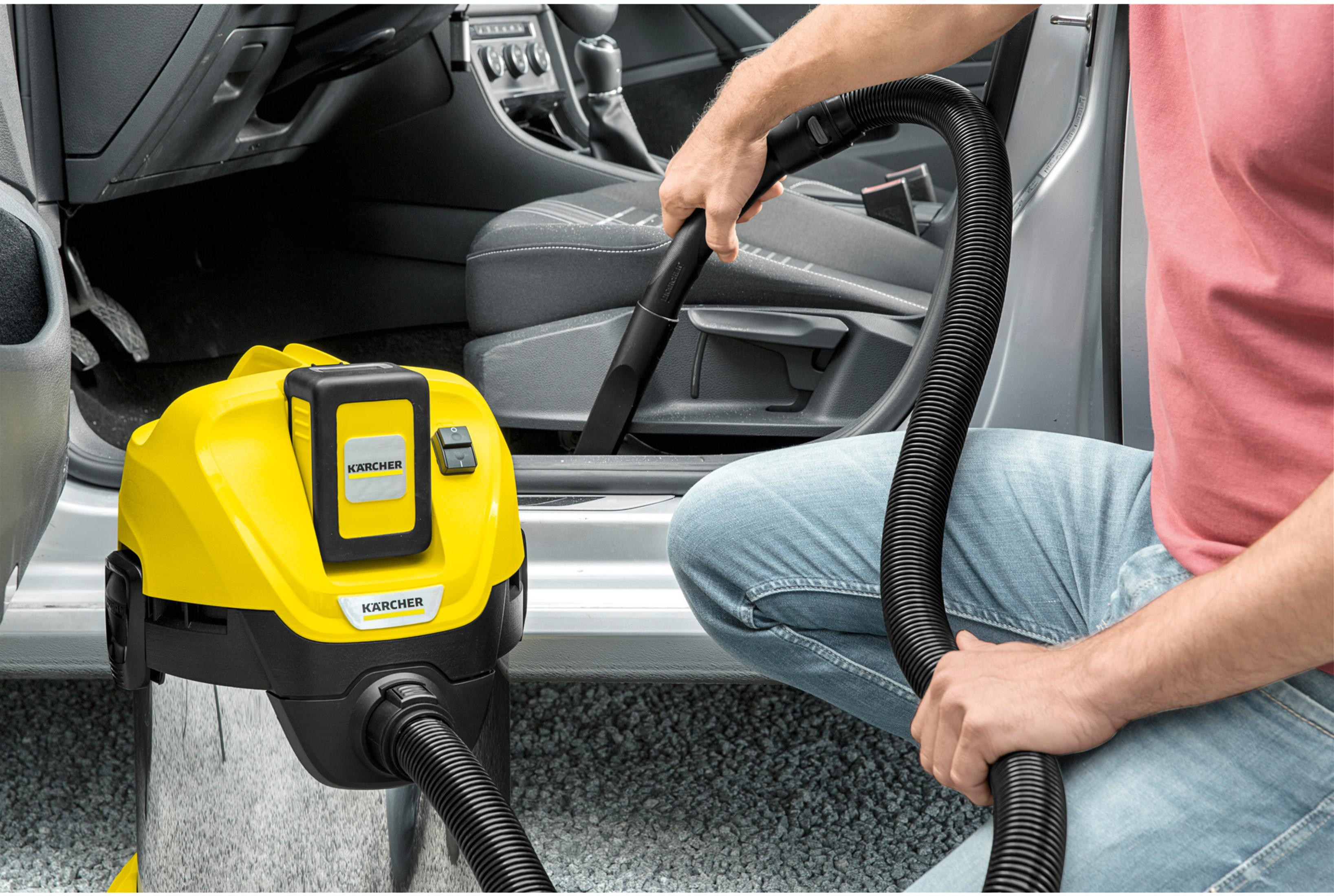 Aspirapolvere Kärcher giallo con tubo in un'auto, persona che pulisce i sedili.