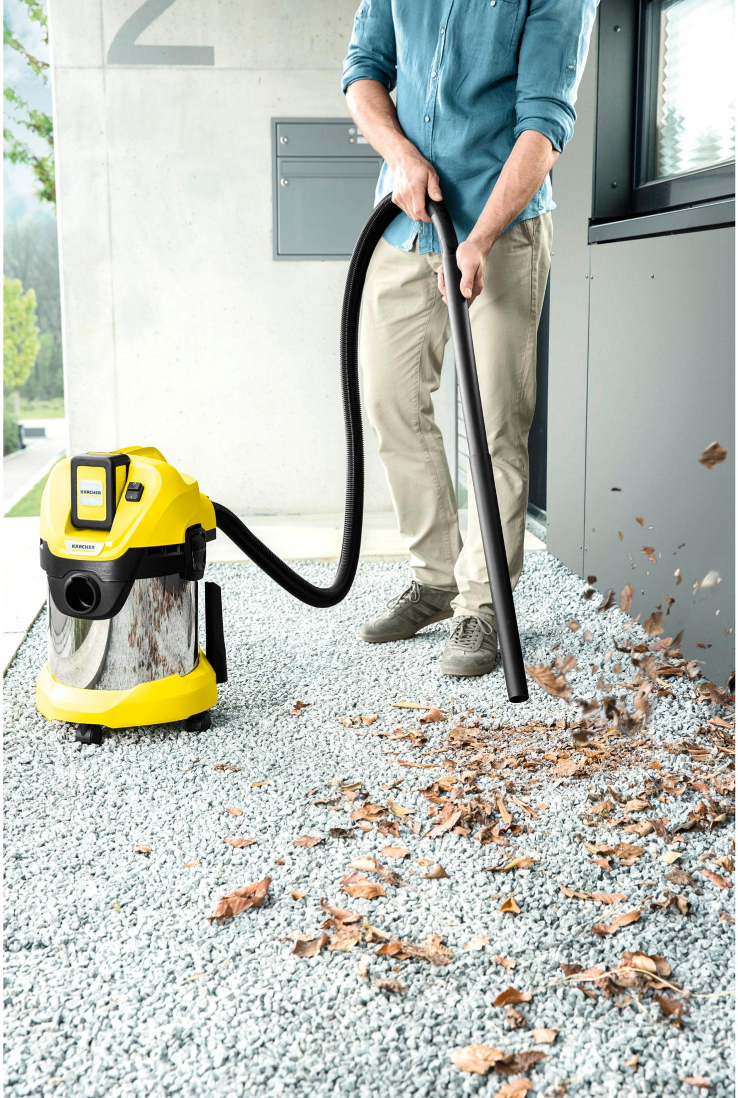 Uomo aspira foglie con aspirapolvere Karcher su vialetto di ghiaia.