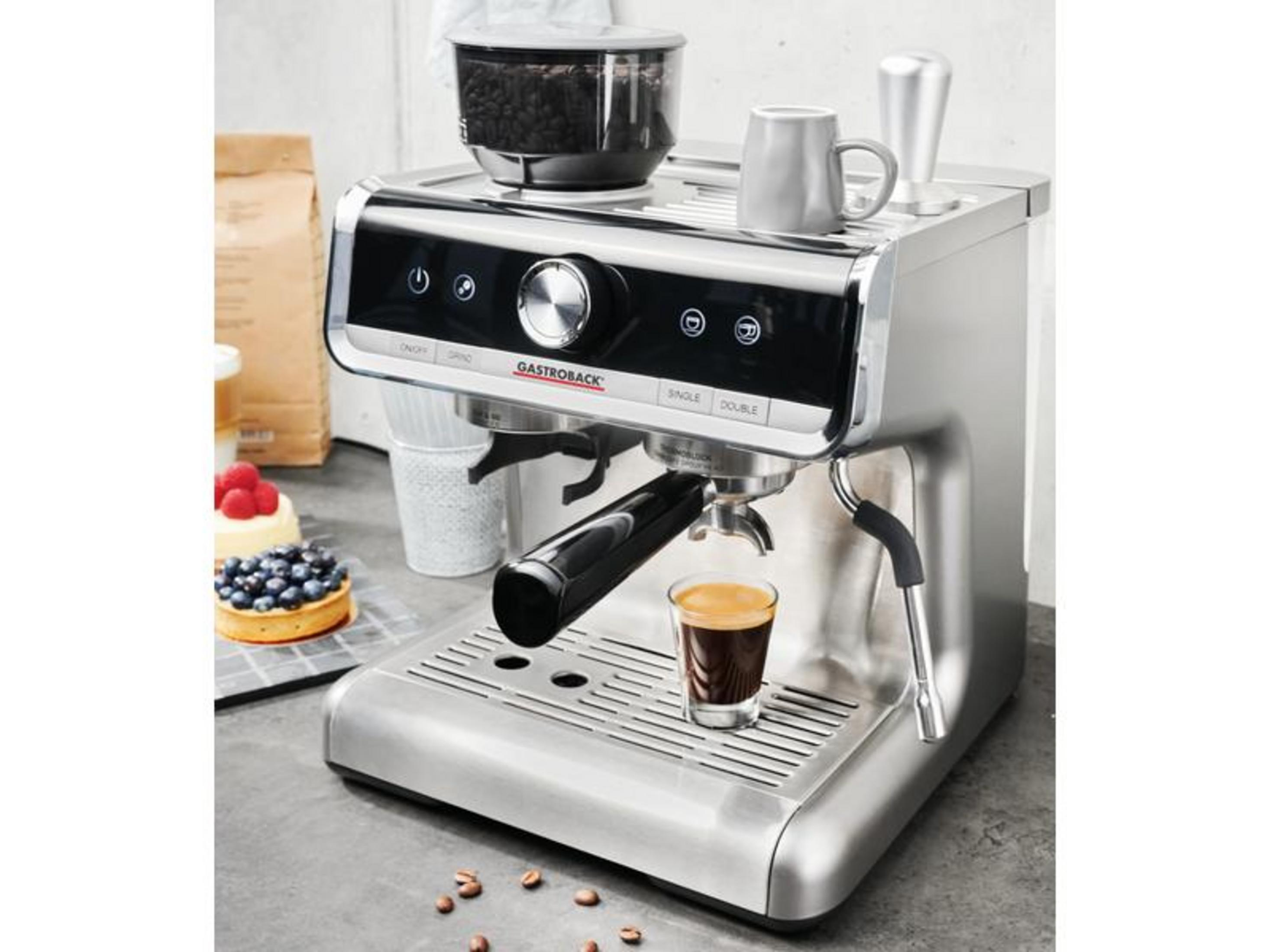 Eine silberne Espressomaschine mit einer Tasse Espresso, Kaffeebohnen und Kuchen.