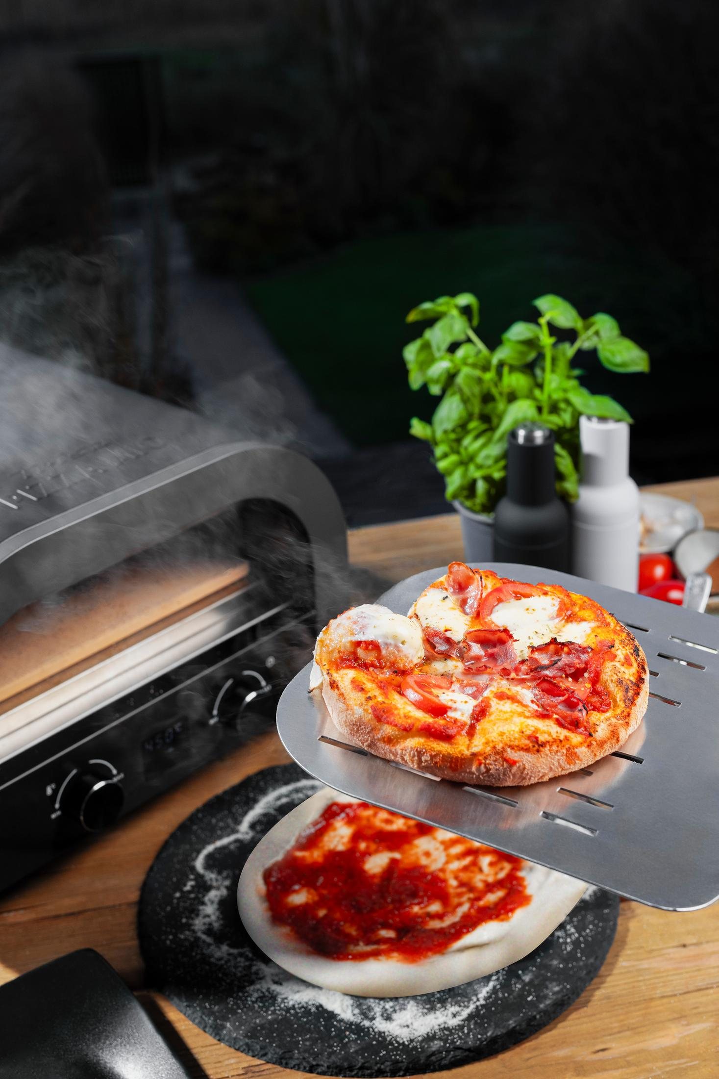 Un four à pizza fumant, une pizza sur une pelle et une pizza crue avec sauce.