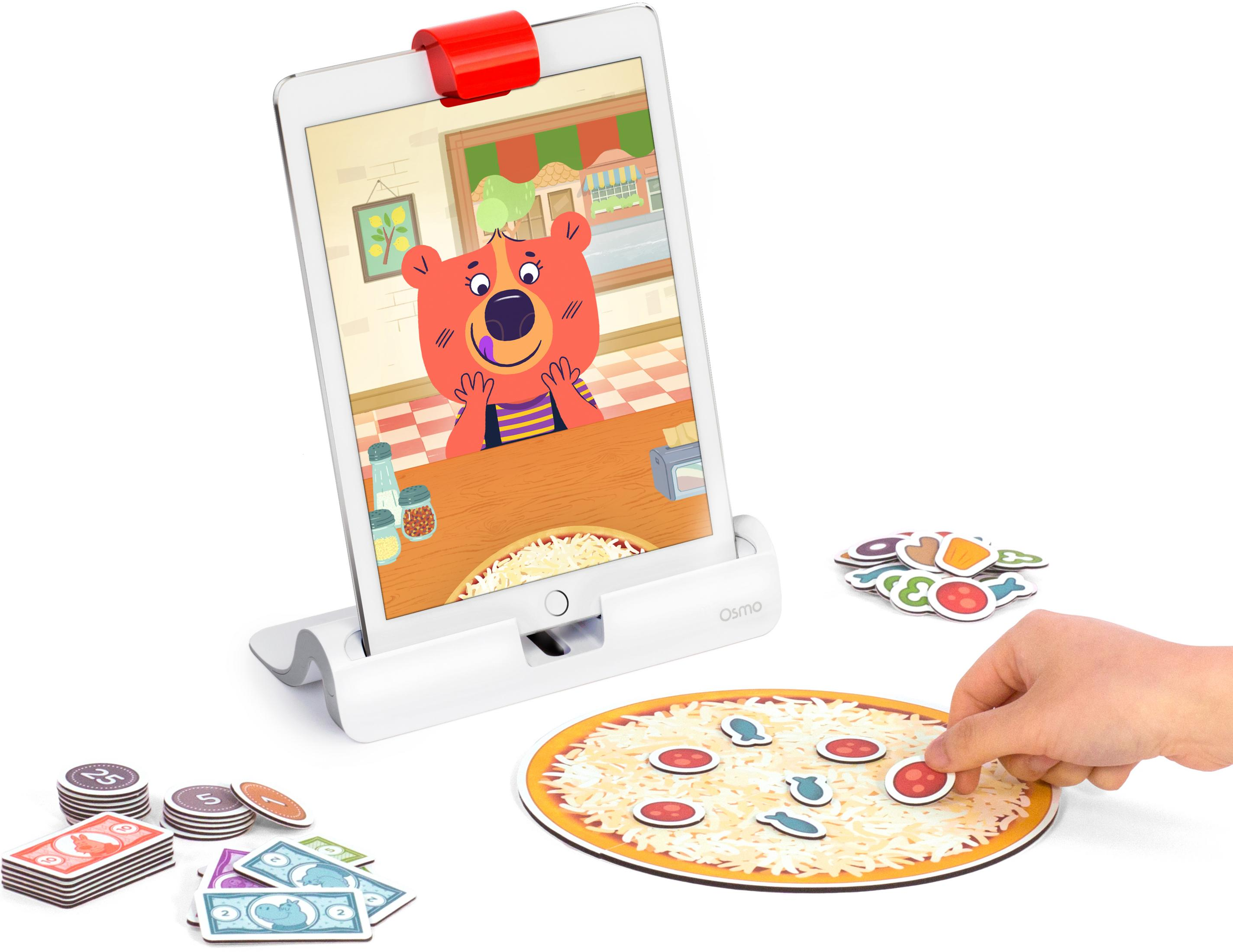 Ein Kind legt Beläge auf eine Pizzaplatte, während auf einem Tablet ein Bär zu sehen ist.
