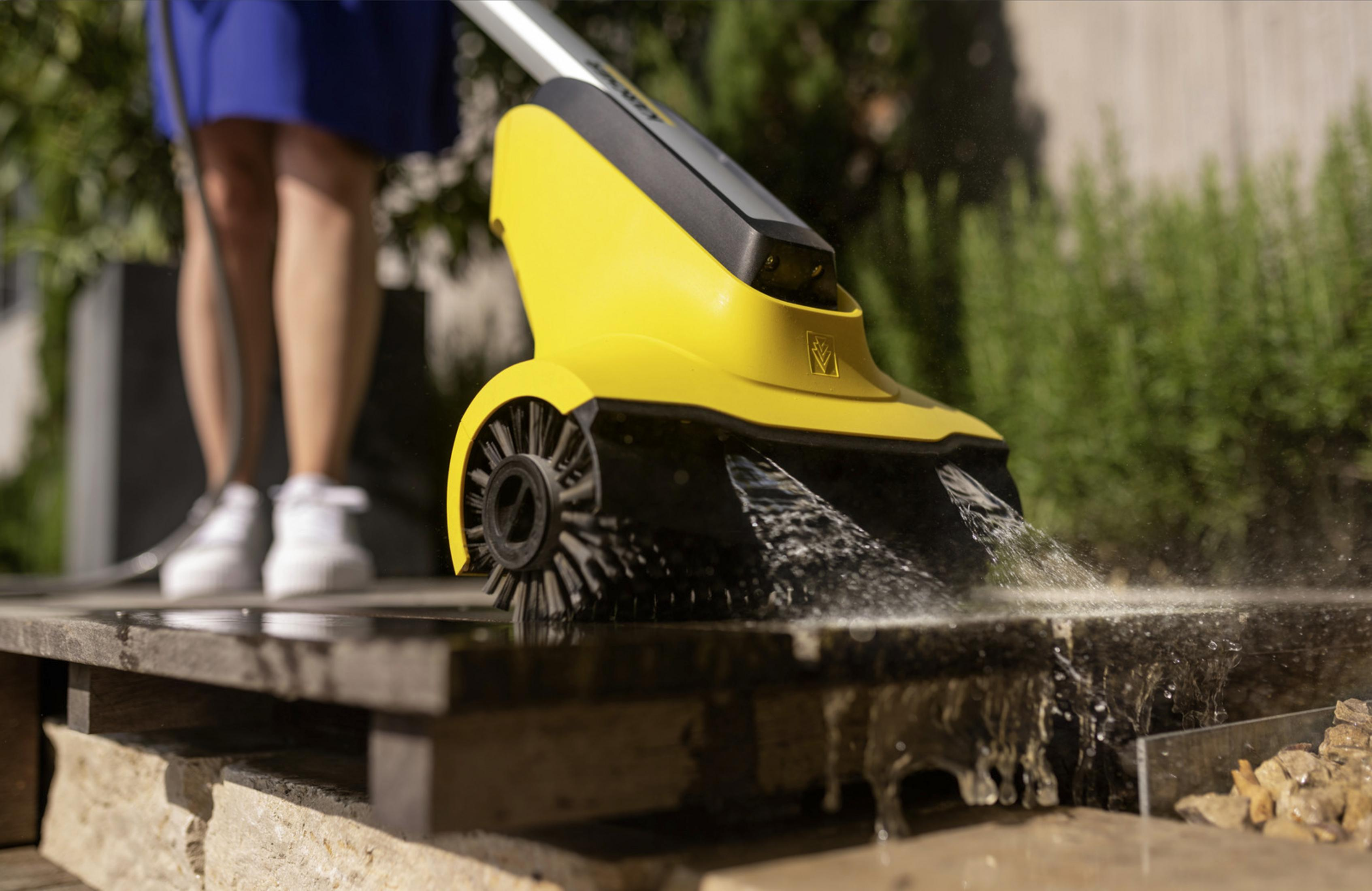 Eine gelbe Reinigungsbürste mit Wasserstrahlen reinigt eine Steinplatte.