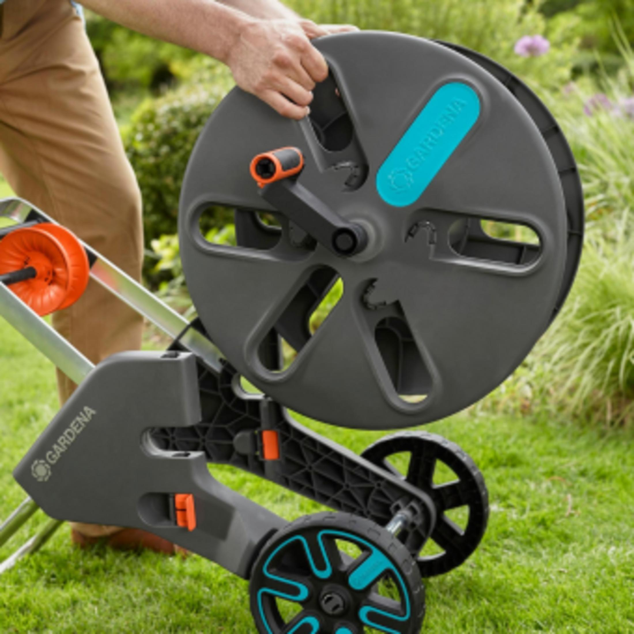 Grauer Gartenschlauchwagen mit orangefarbenem Griff und Rädern.
