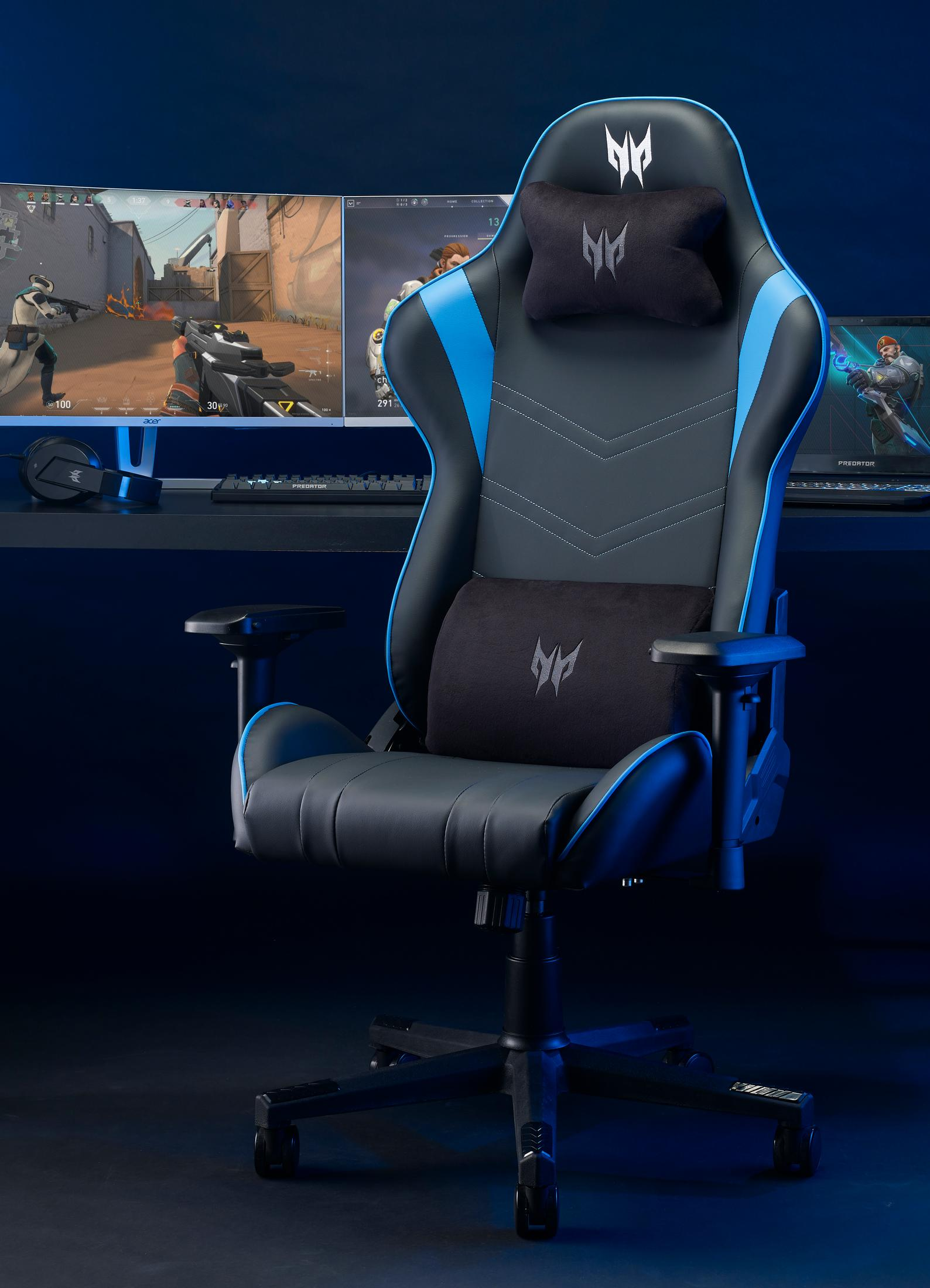 Una sedia da gaming nera e blu con cuscini lombare e poggiatesta si trova davanti a più monitor.