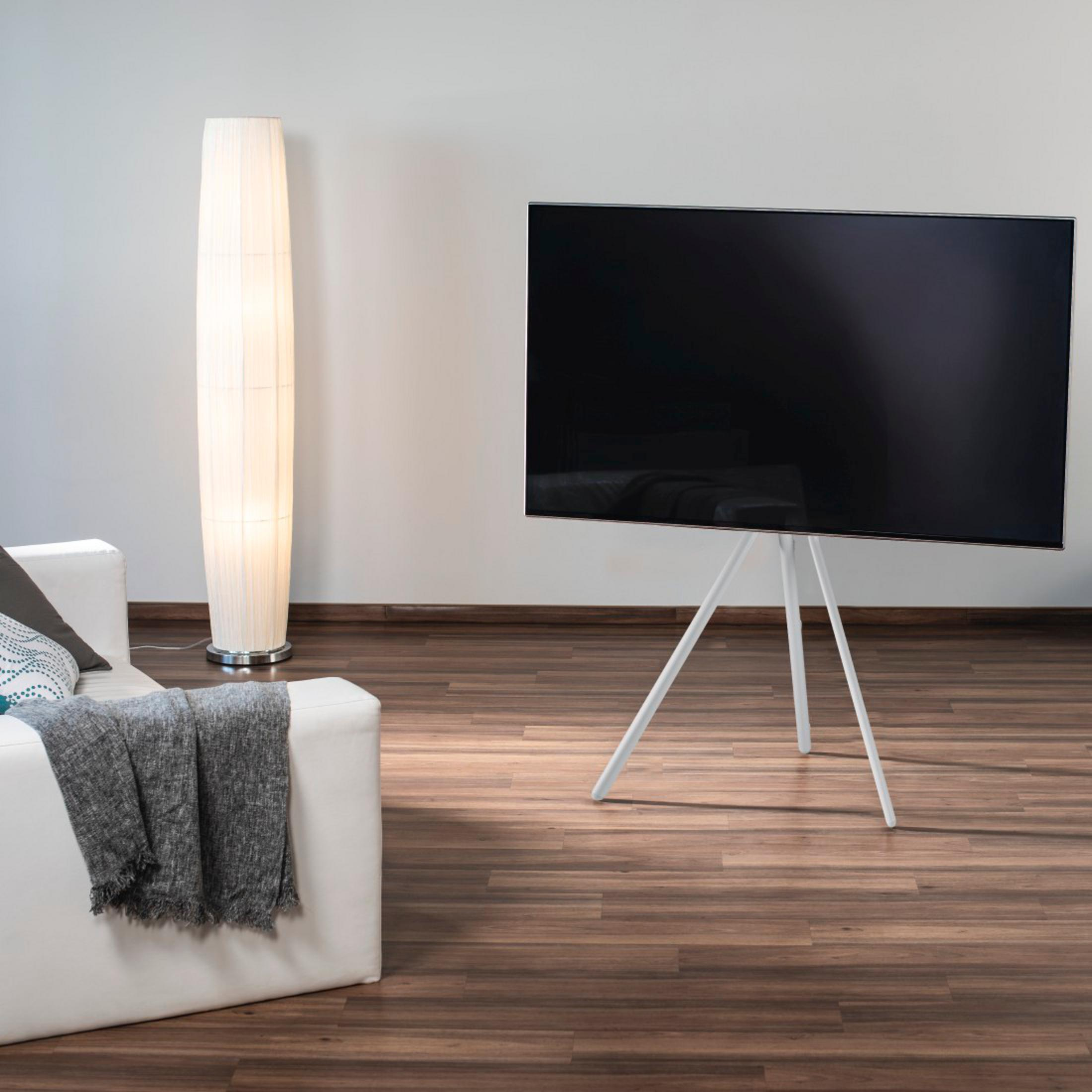 Ein weier Fernseher auf einem weien Stativ neben einem Sofa und einer Stehlampe.