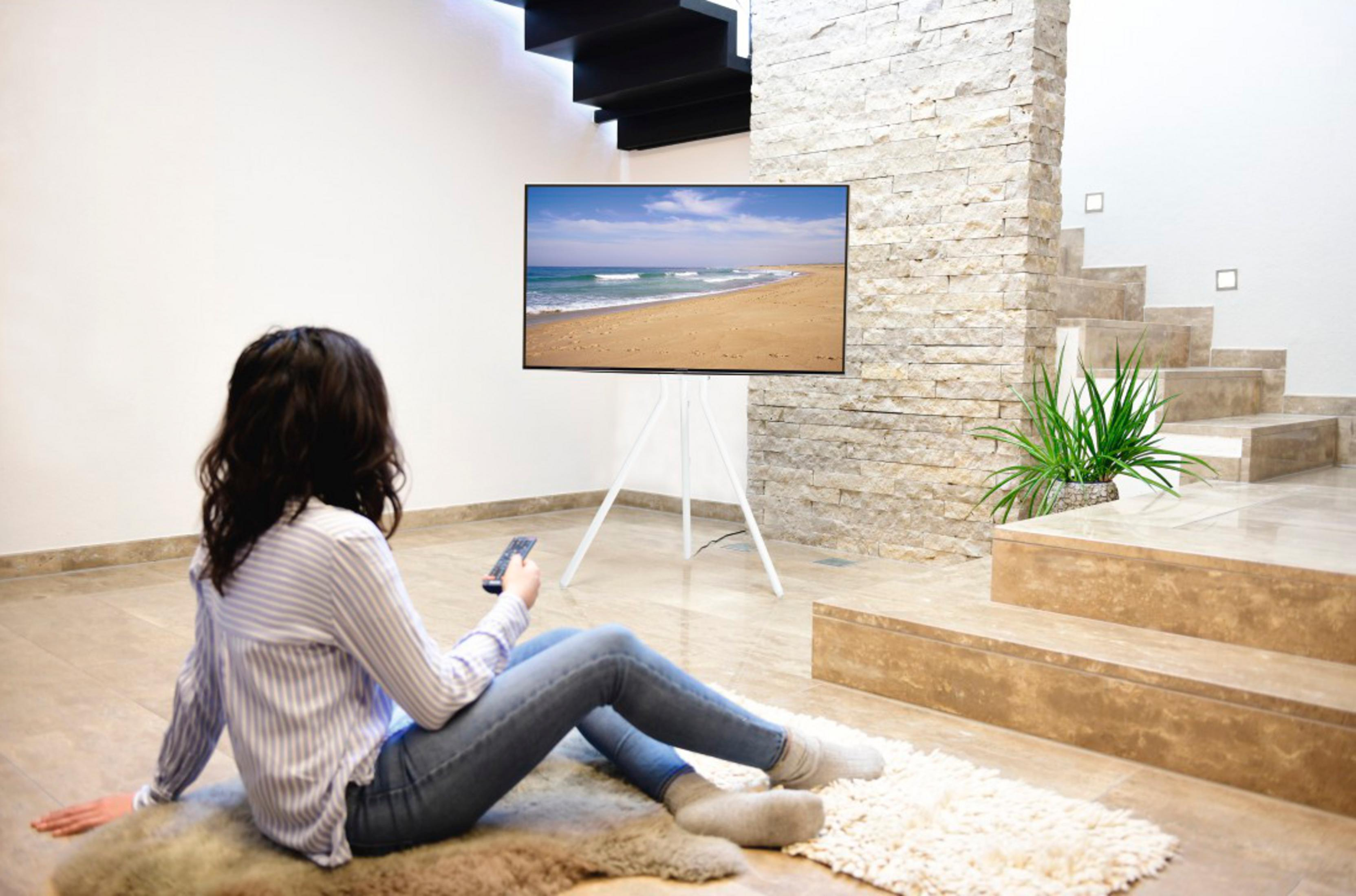 Eine Frau sitzt auf einem Teppich vor einem Fernseher, der einen Strand zeigt.
