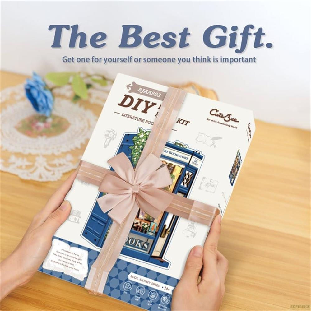 Hände halten ein geschenkverpacktes DIY-Buchnischen-Kit mit einer Miniatur-Buchladenszene.