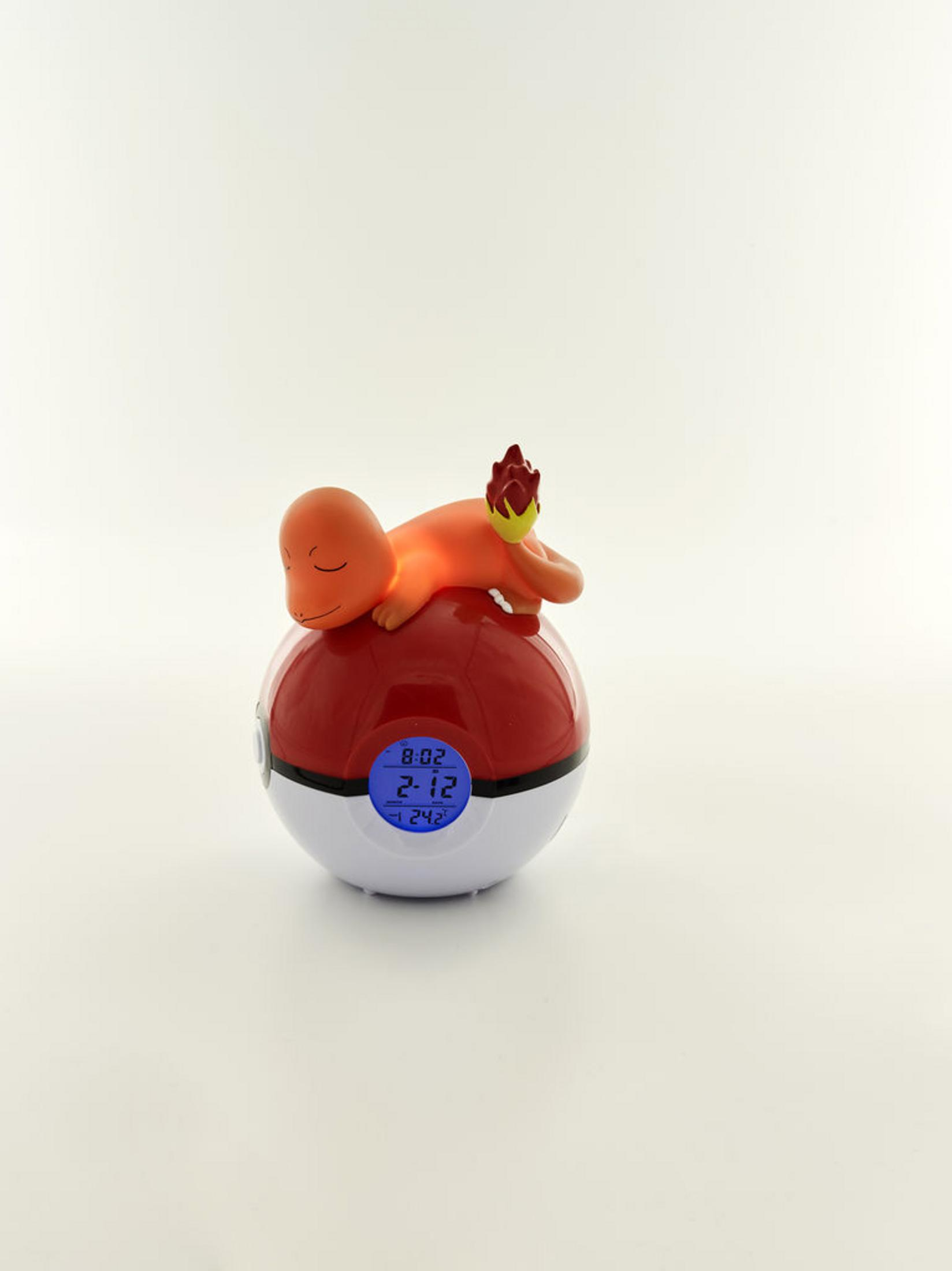 Ein orangefarbener Charmander schläft auf einem Pokéball-Wecker mit blauem Display.