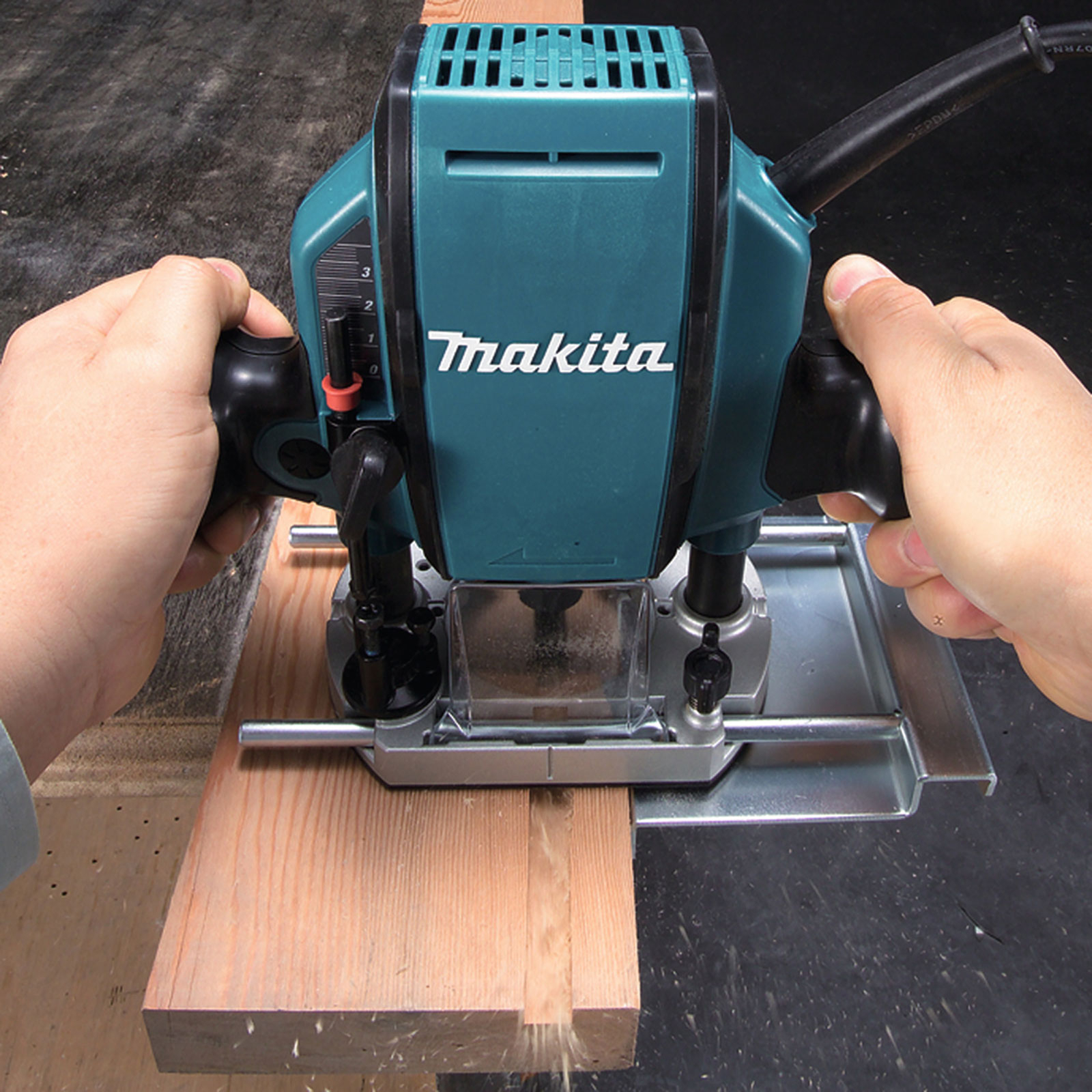 Hände führen eine Makita-Oberfräse über ein Holzstück, Staub fliegt auf.