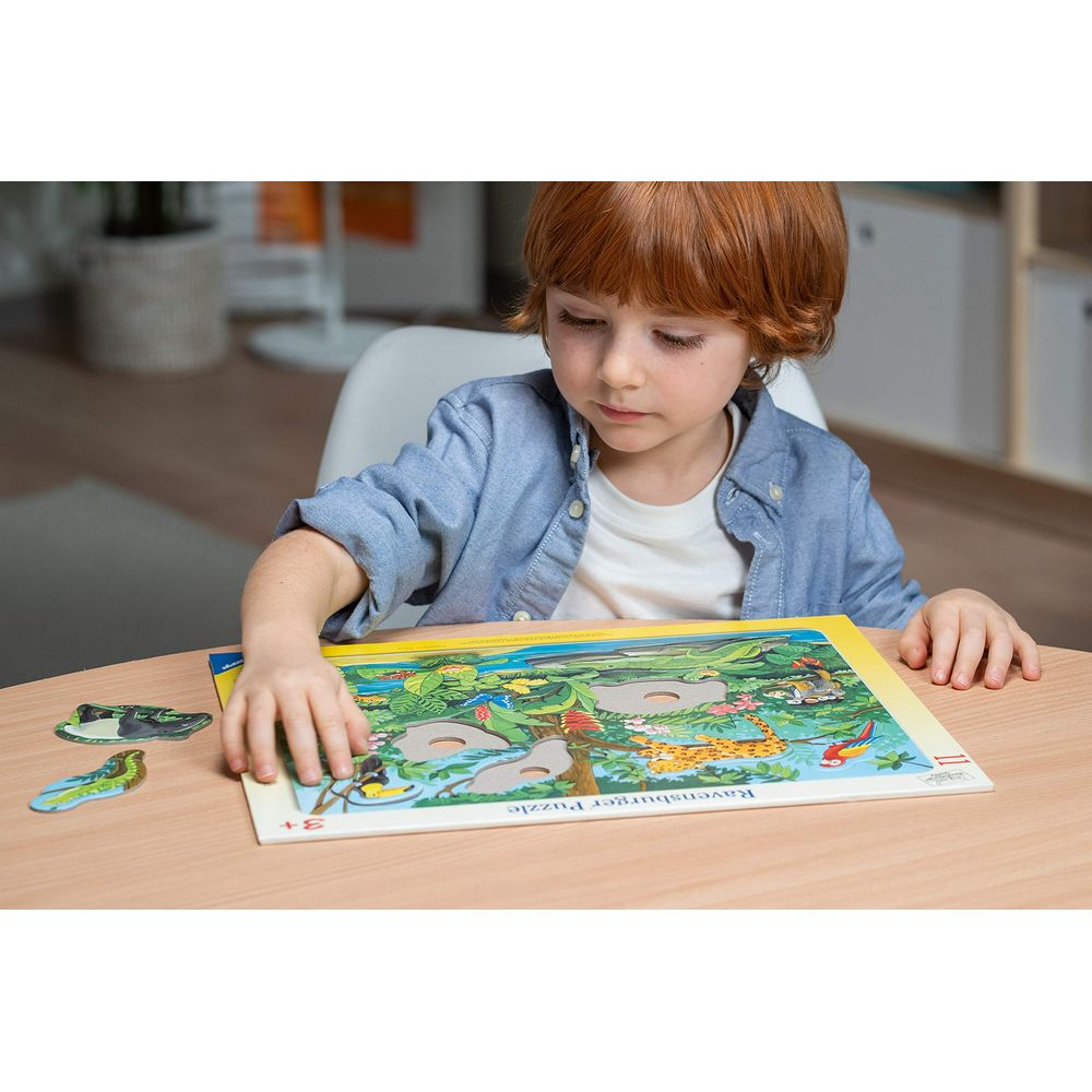 Un bambino dai capelli rossi lavora a un puzzle Ravensburger a tema giungla.