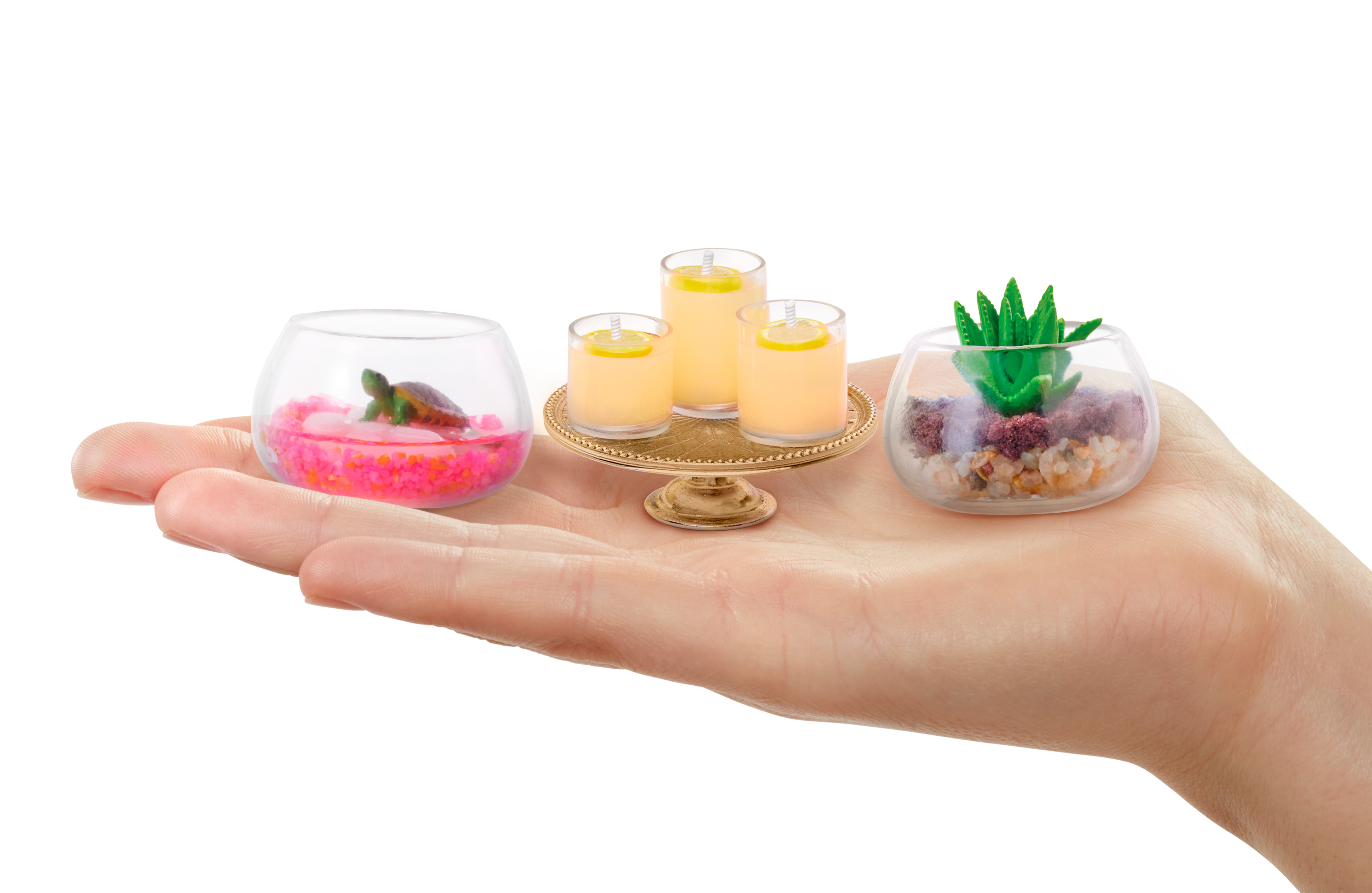 Eine Hand hält drei Miniatur-Dekorationen: Schildkröte im Tank, Kerzen und Sukkulente.