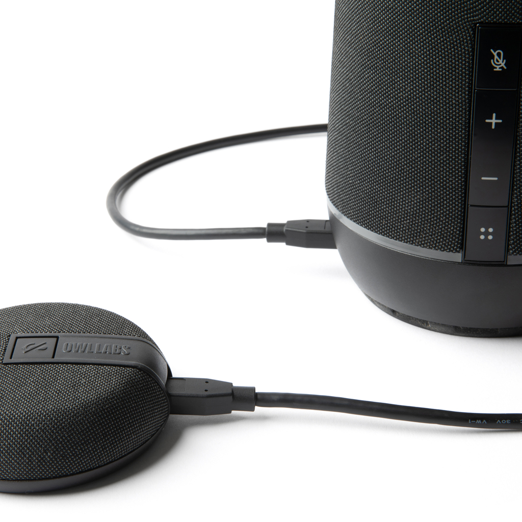 Altavoz y micrófono redondos Owl Labs negros conectados por cables USB sobre fondo blanco.