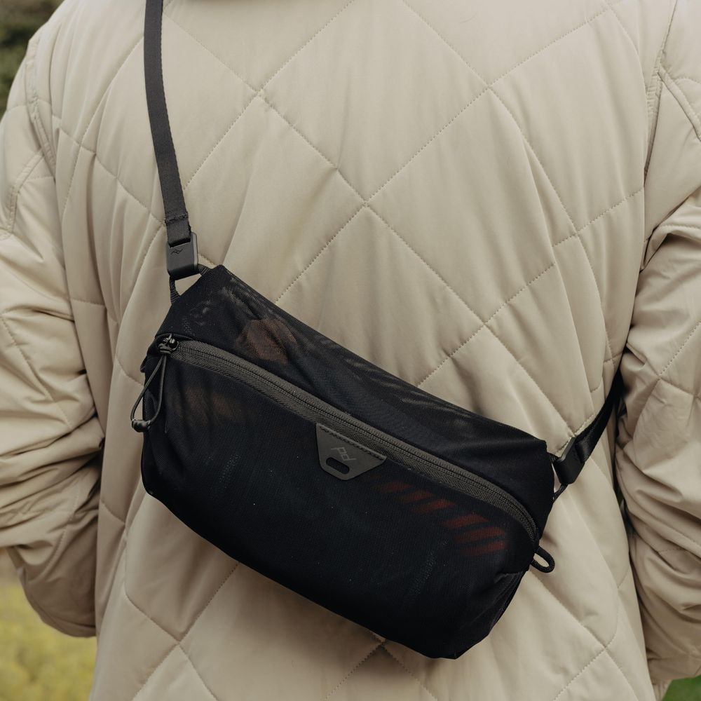 Een persoon draagt een gewatteerde beige jas met een zwarte mesh schoudertas.