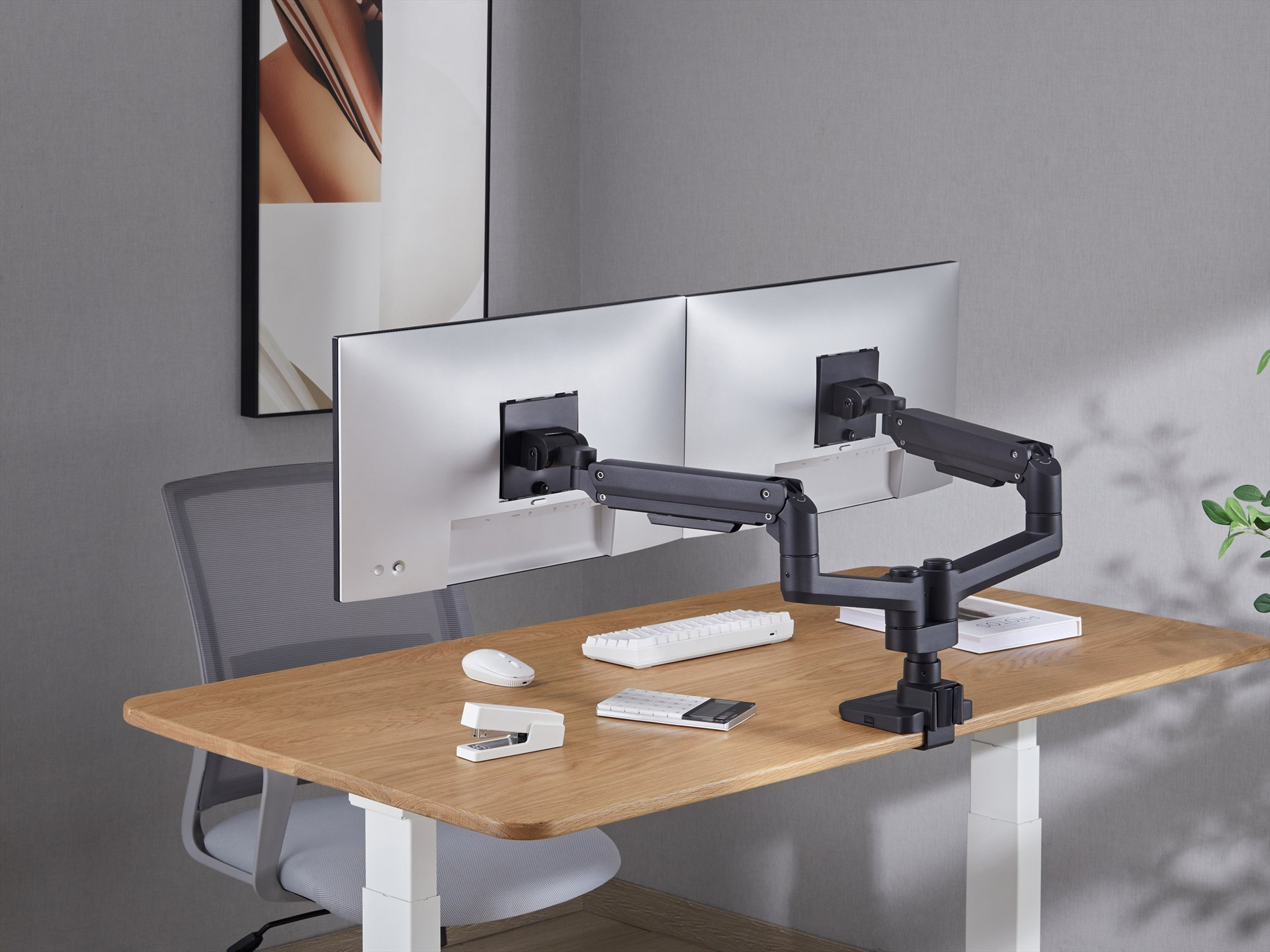 Ein Schreibtisch mit zwei Monitoren, die an einem schwarzen Arm befestigt sind. Eine Maus, Tastatur und ein Tacker liegen auf dem Tisch.