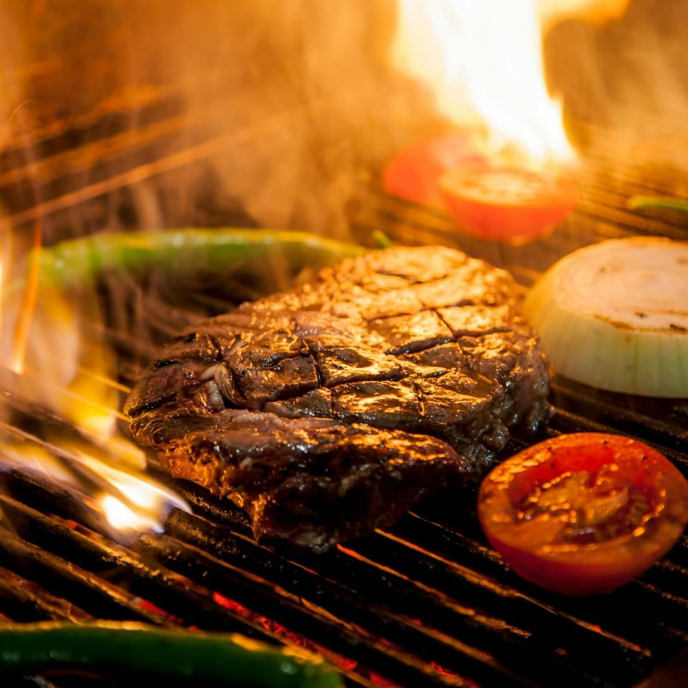 Una bistecca viene grigliata con pomodori, cipolle e peperoni sul fuoco.