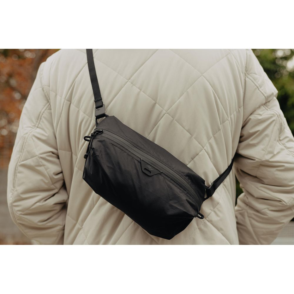 Persoon in gewatteerde jas met zwarte crossbody tas. Buiten.