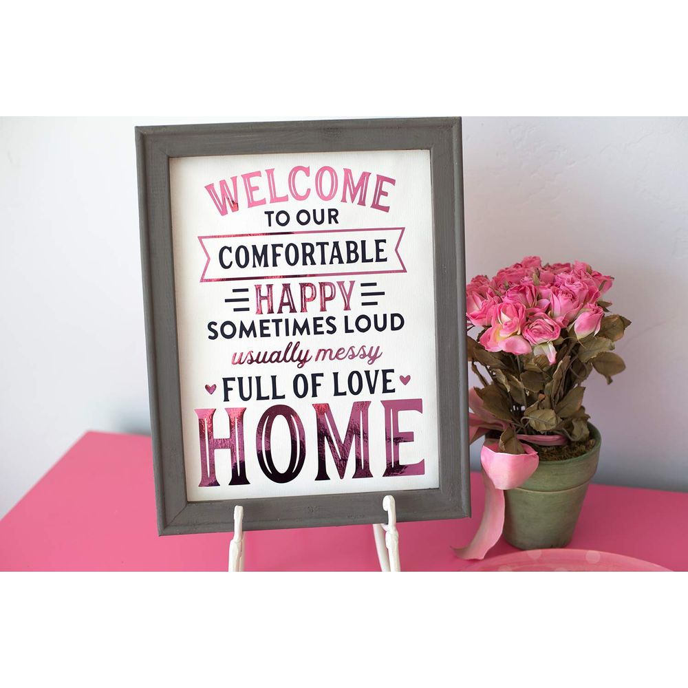 Ein gerahmtes Schild mit Text über Zuhause, daneben eine Topfpflanze mit rosa Rosen.